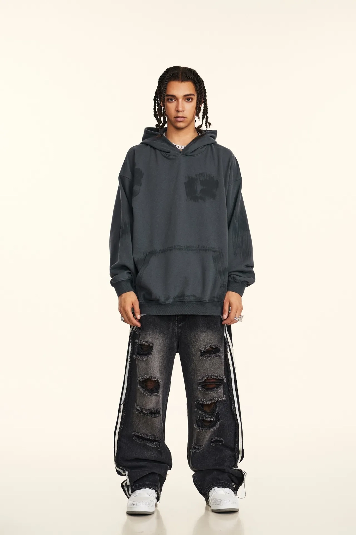 Person wearing a dark gray hoodie and distressed jeans on a white background