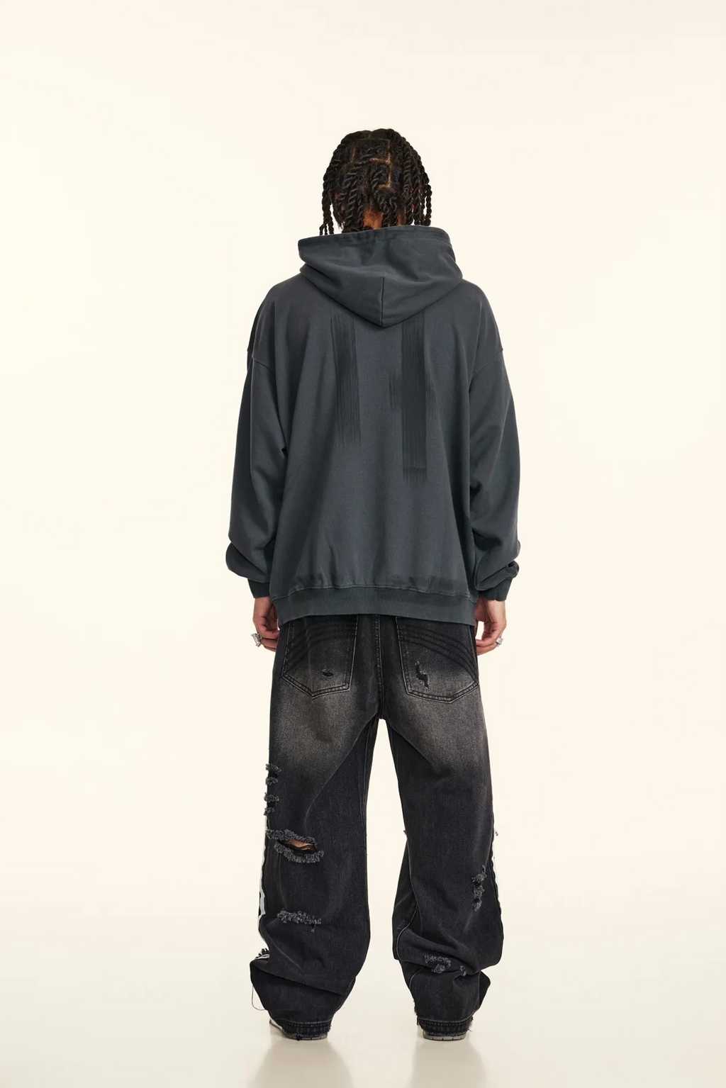 Person wearing a dark gray hoodie and black distressed jeans on a white background