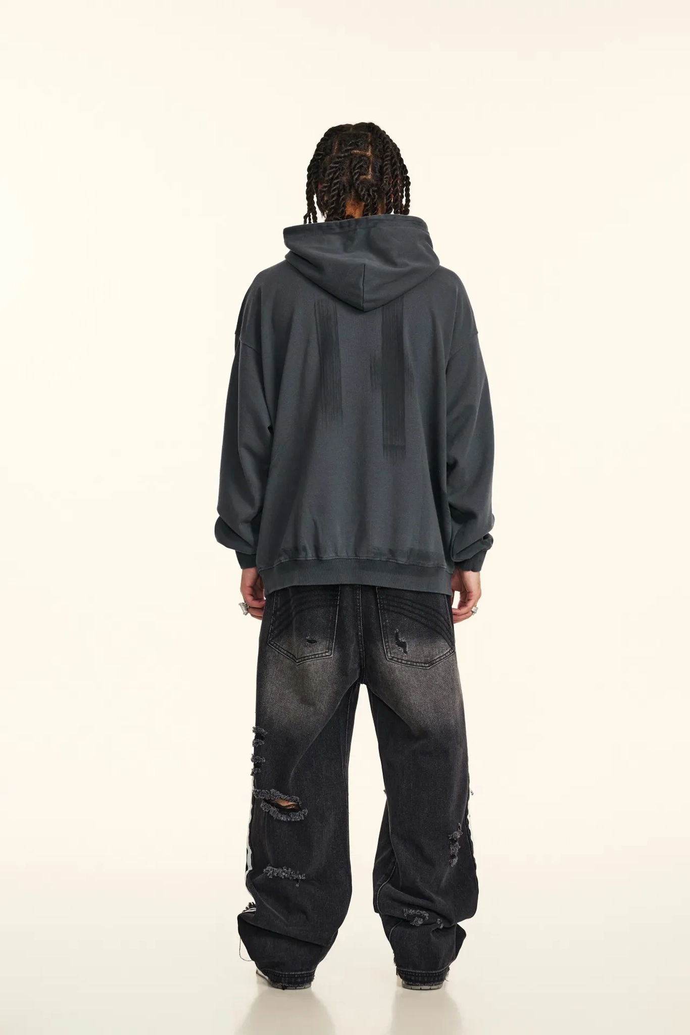 Person wearing a dark gray hoodie and black distressed jeans on a white background