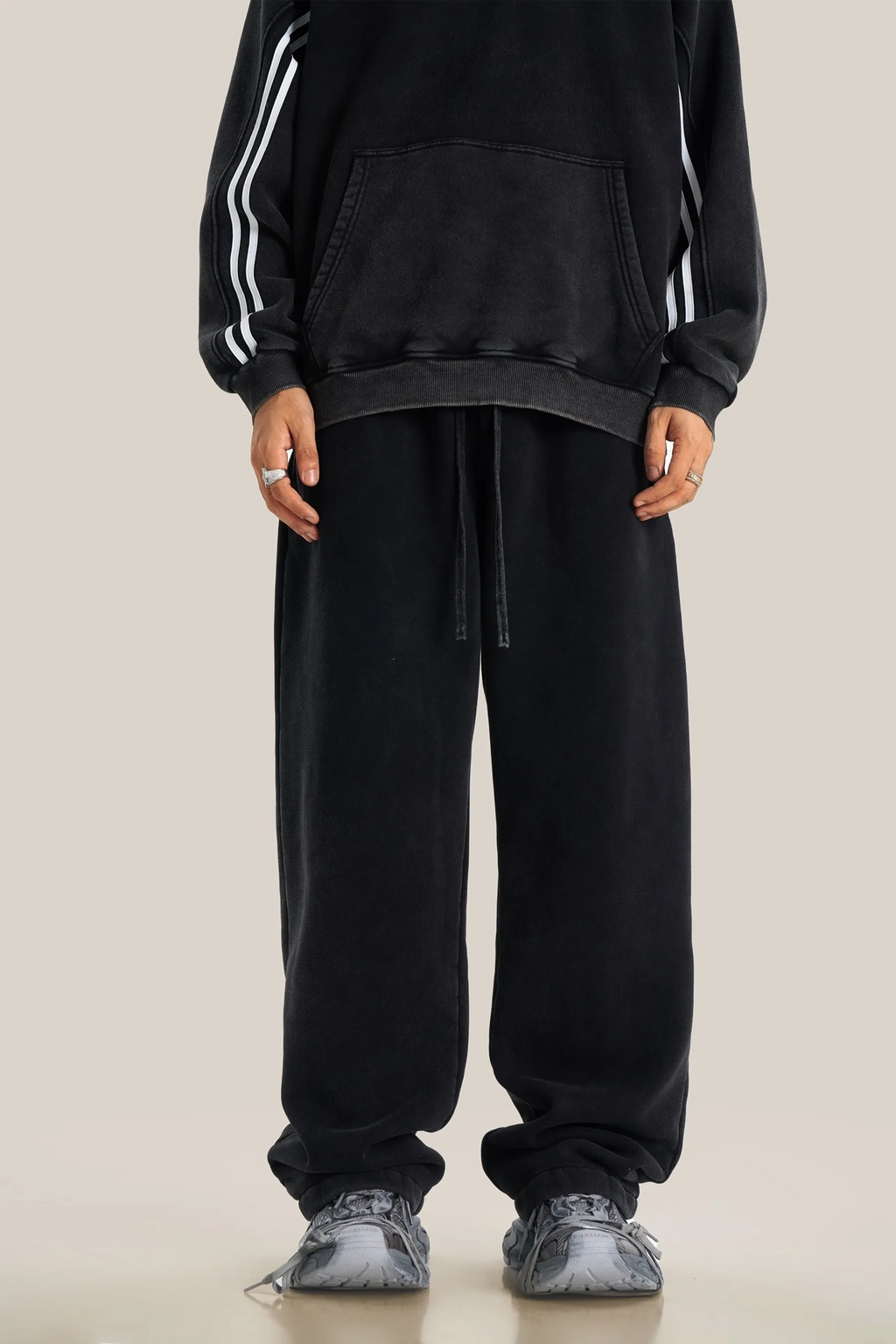 Person wearing a black tracksuit with white stripes on a beige background