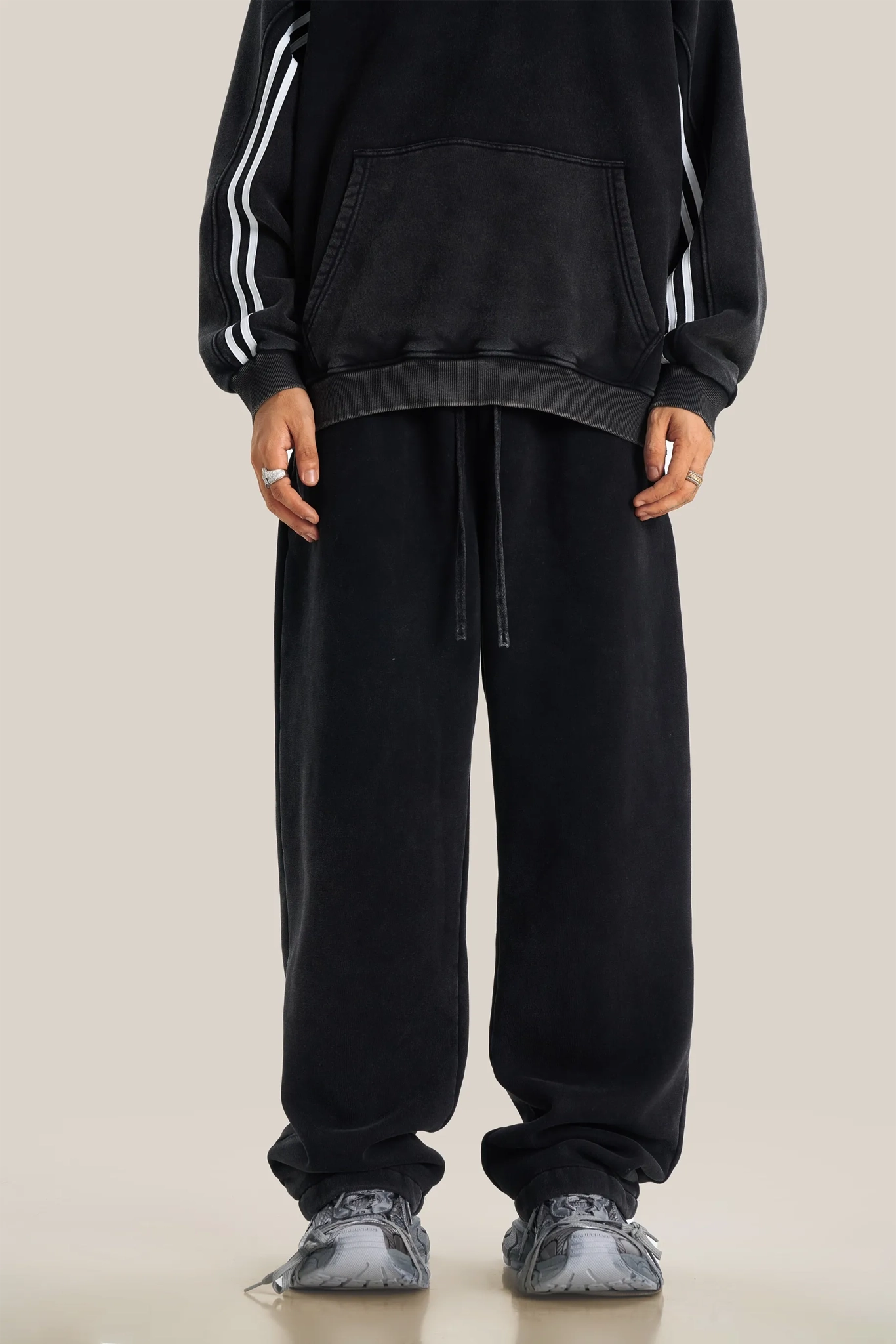 Person wearing a black tracksuit with white stripes on a beige background