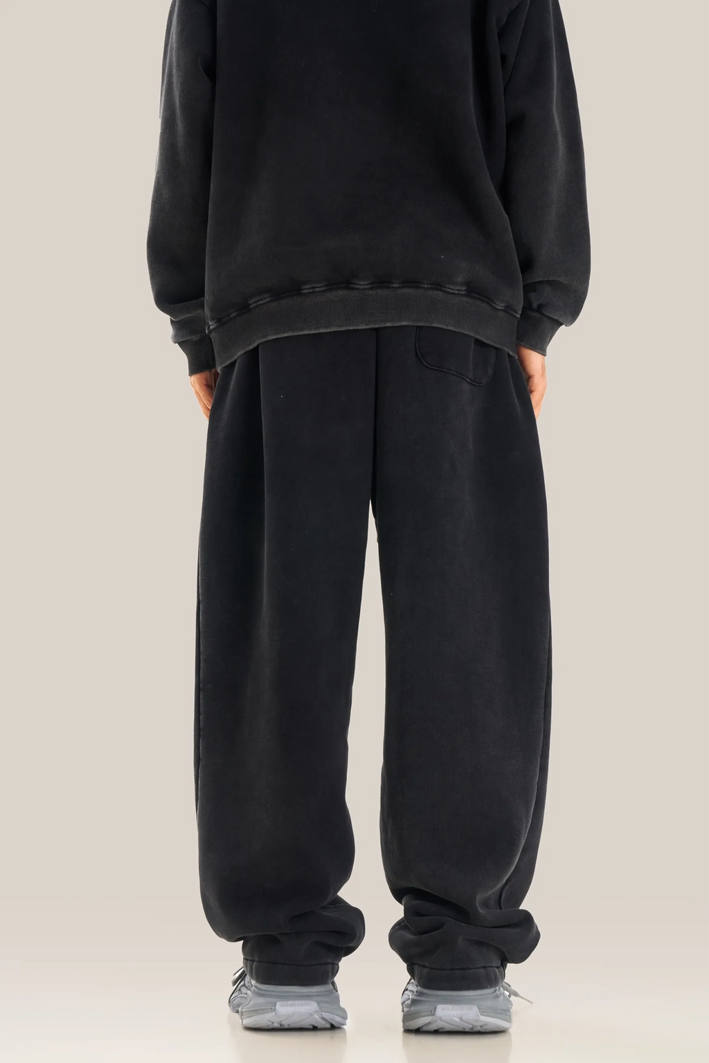 Person wearing a black oversized sweatshirt and pants on a beige background