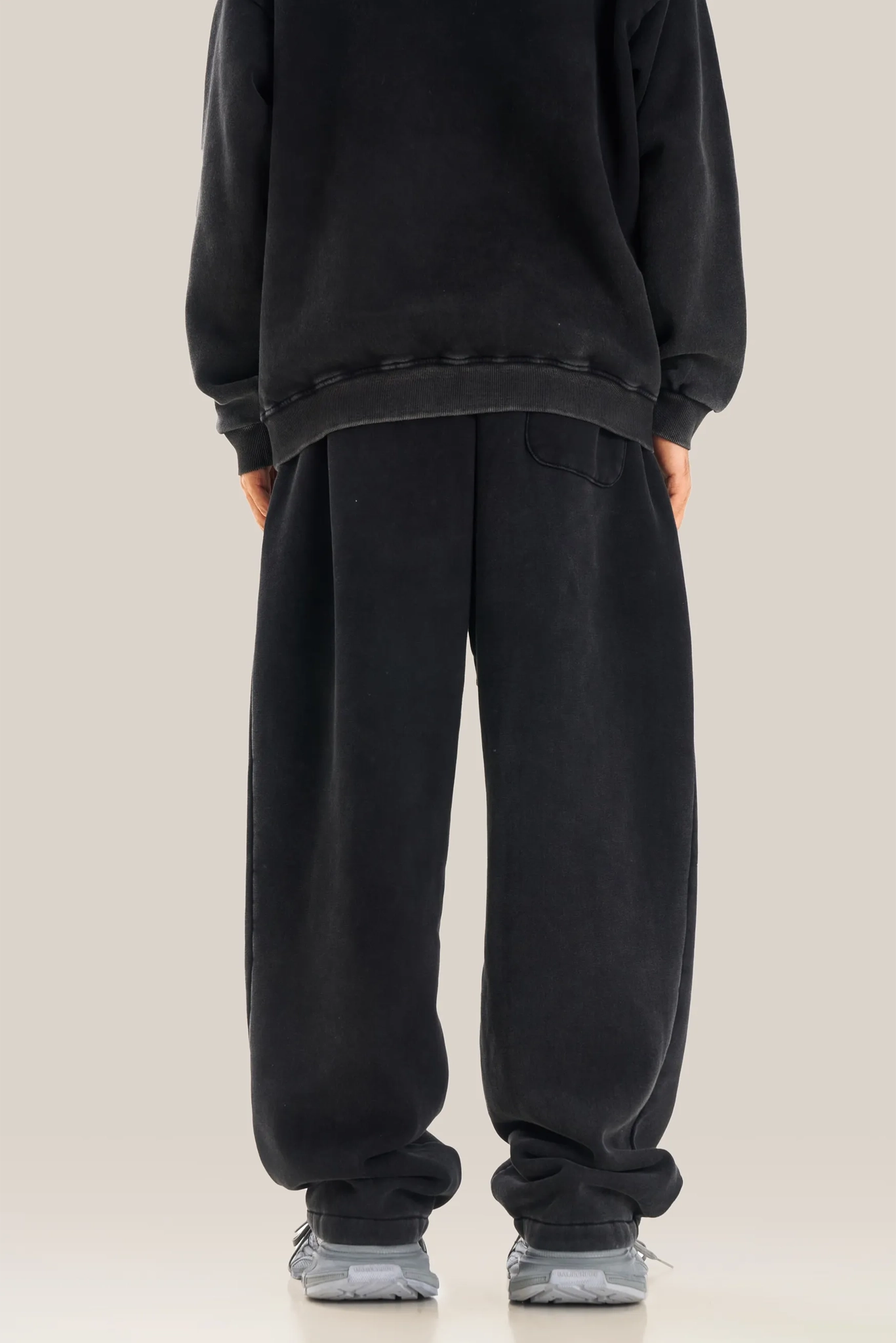Person wearing a black oversized sweatshirt and pants on a beige background