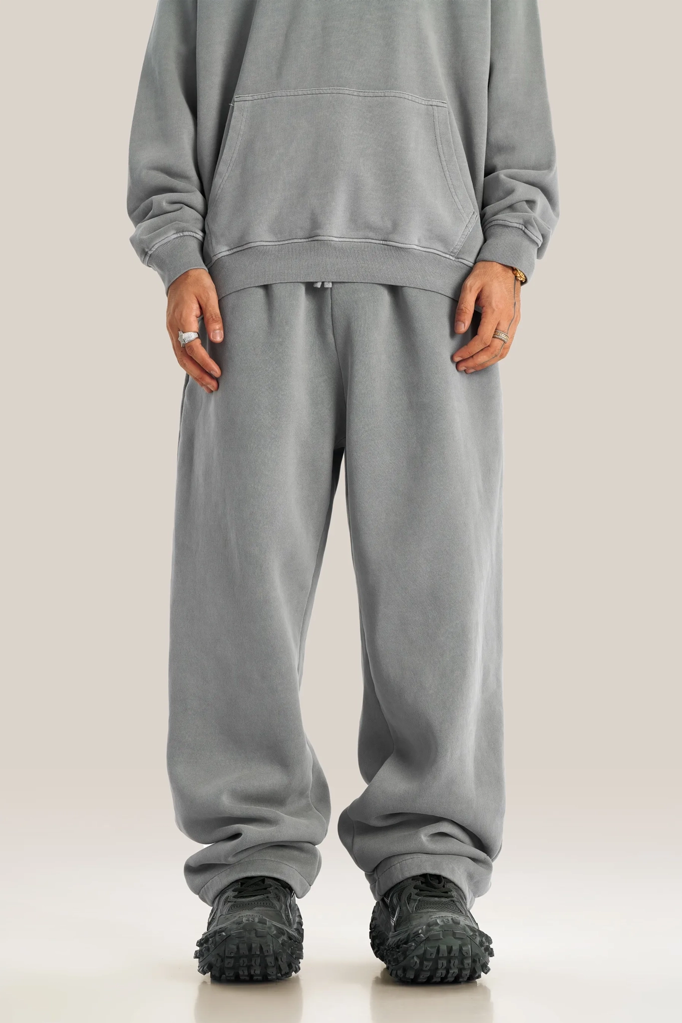 Person wearing a gray hoodie and sweatpants with black shoes on a light background