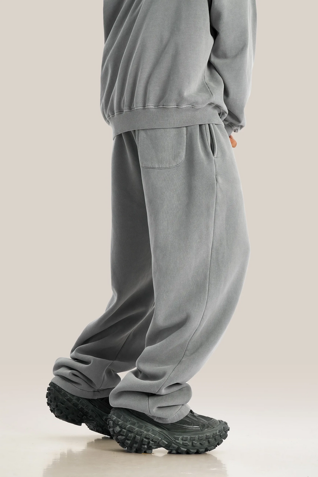Person wearing gray sweatpants and black shoes on a beige background