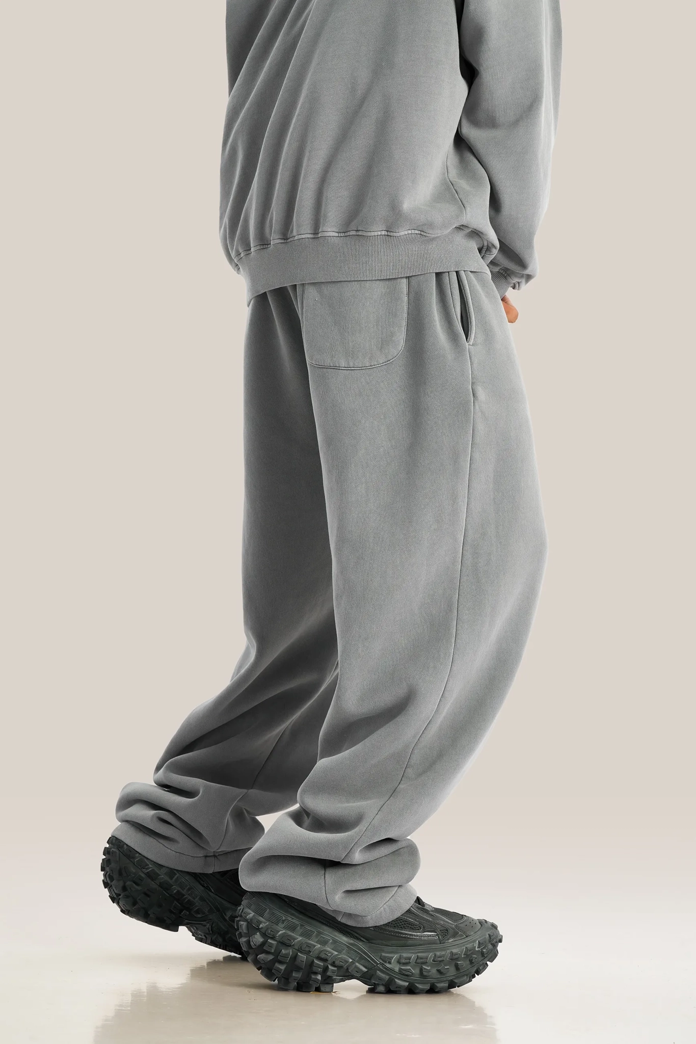 Person wearing gray sweatpants and black shoes on a beige background