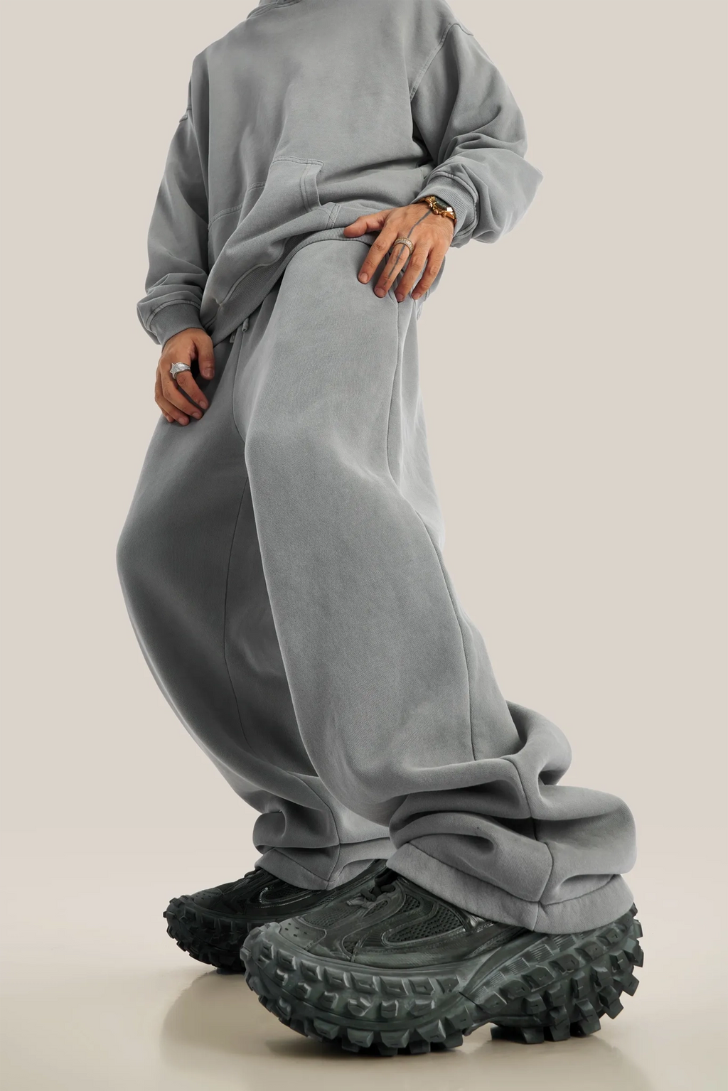 Person wearing a gray sweatshirt and pants with chunky black shoes on a beige background