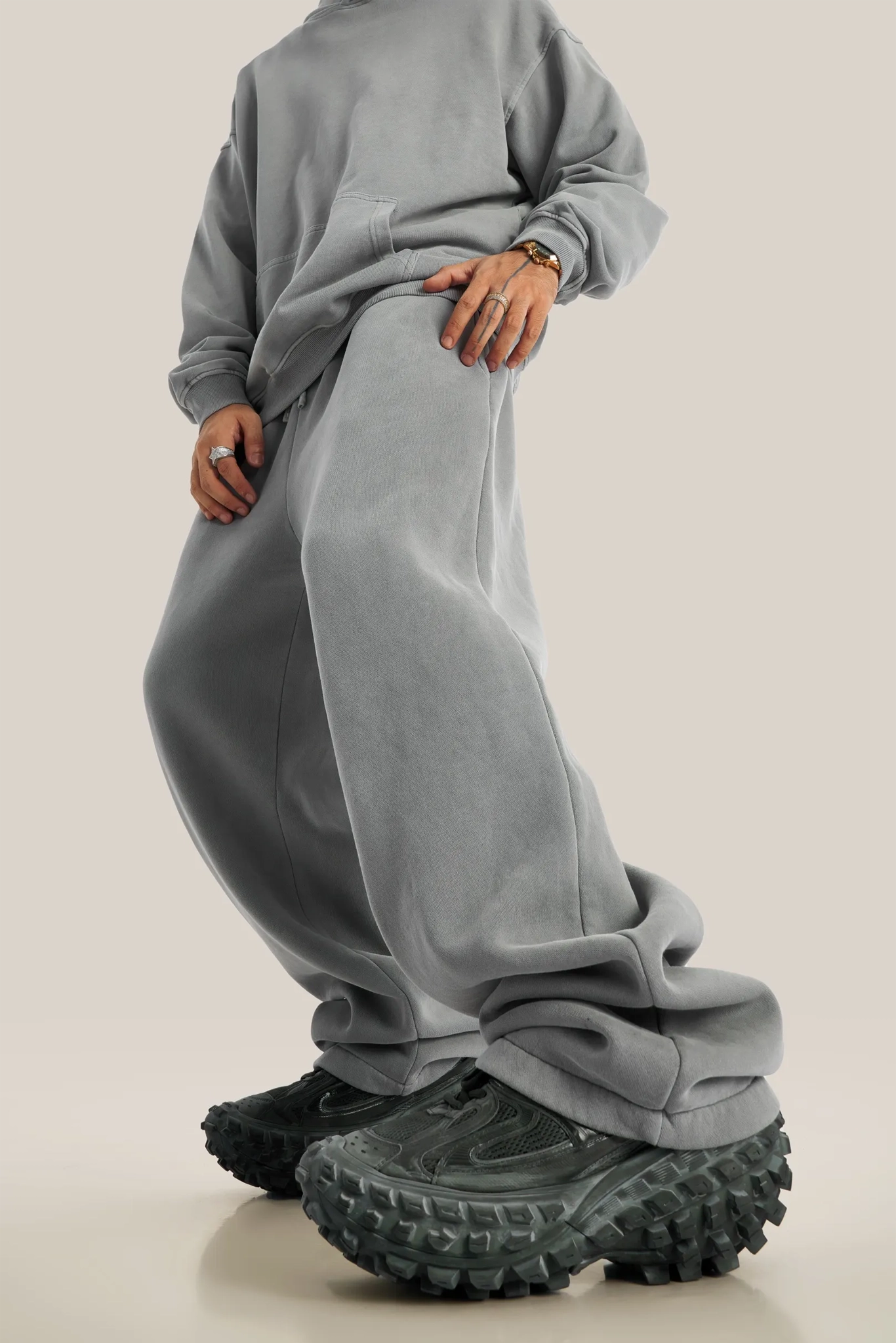 Person wearing a gray sweatshirt and pants with chunky black shoes on a beige background