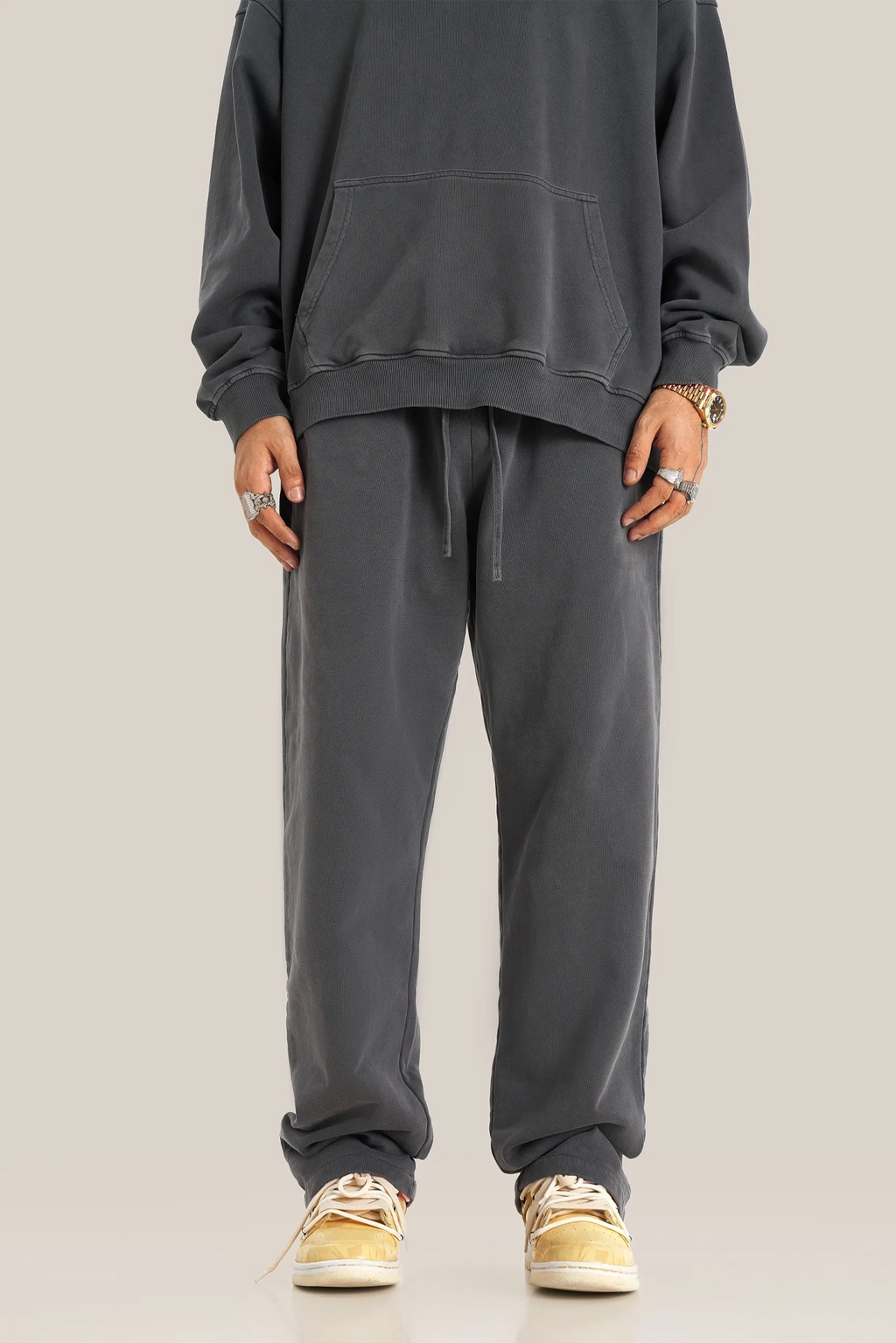 Person wearing a gray tracksuit with beige sneakers on a plain background