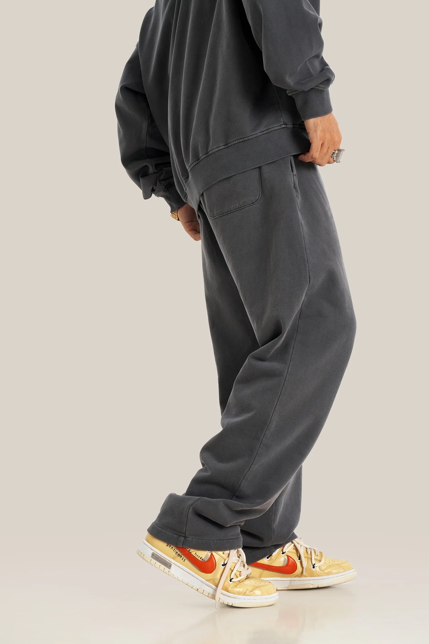 Person wearing dark gray sweatpants and a matching hoodie on a light beige background