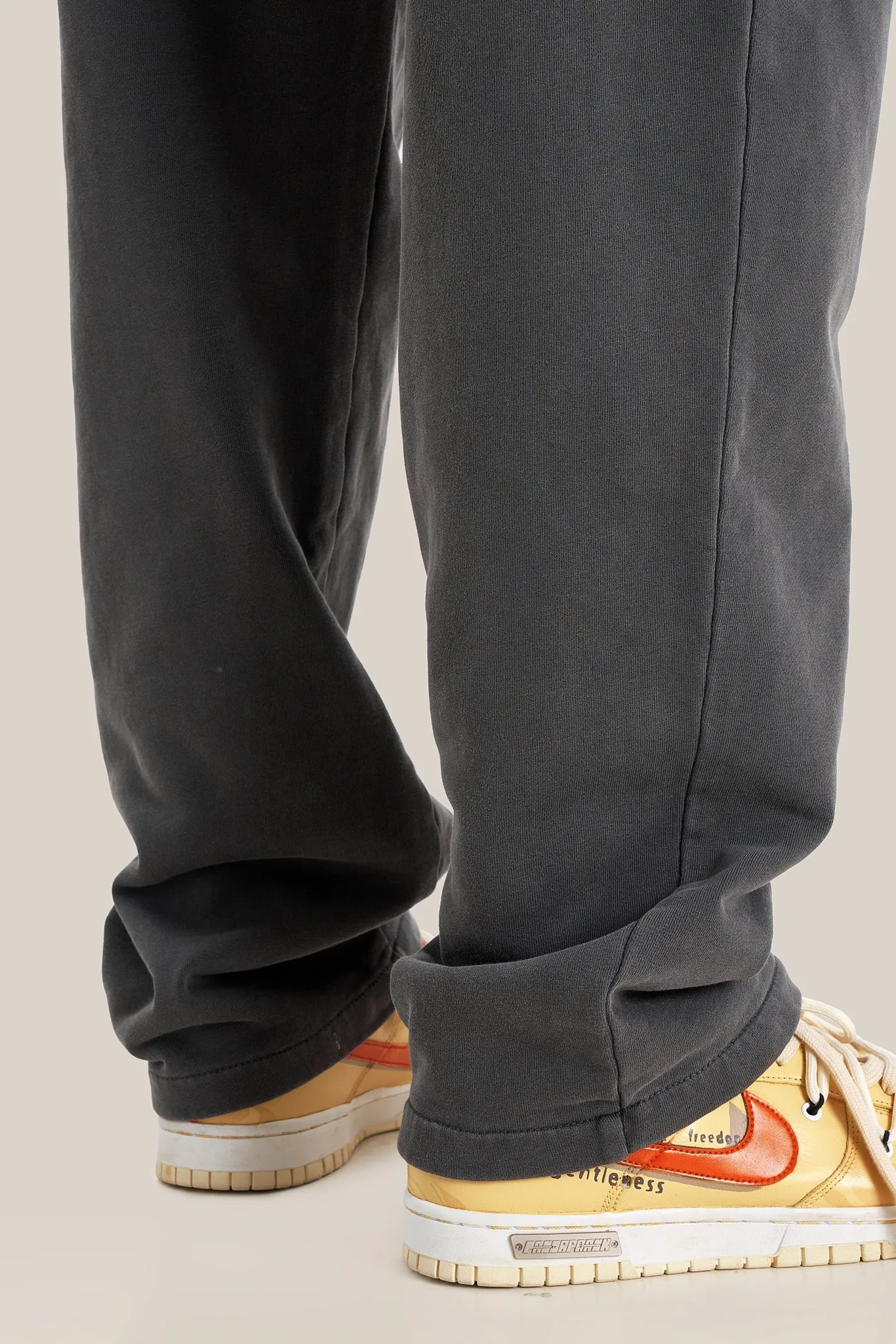 Dark gray pants with a person wearing beige sneakers on a neutral background