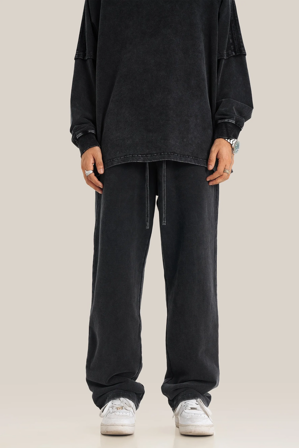 Person wearing a black oversized shirt and black pants on a beige background