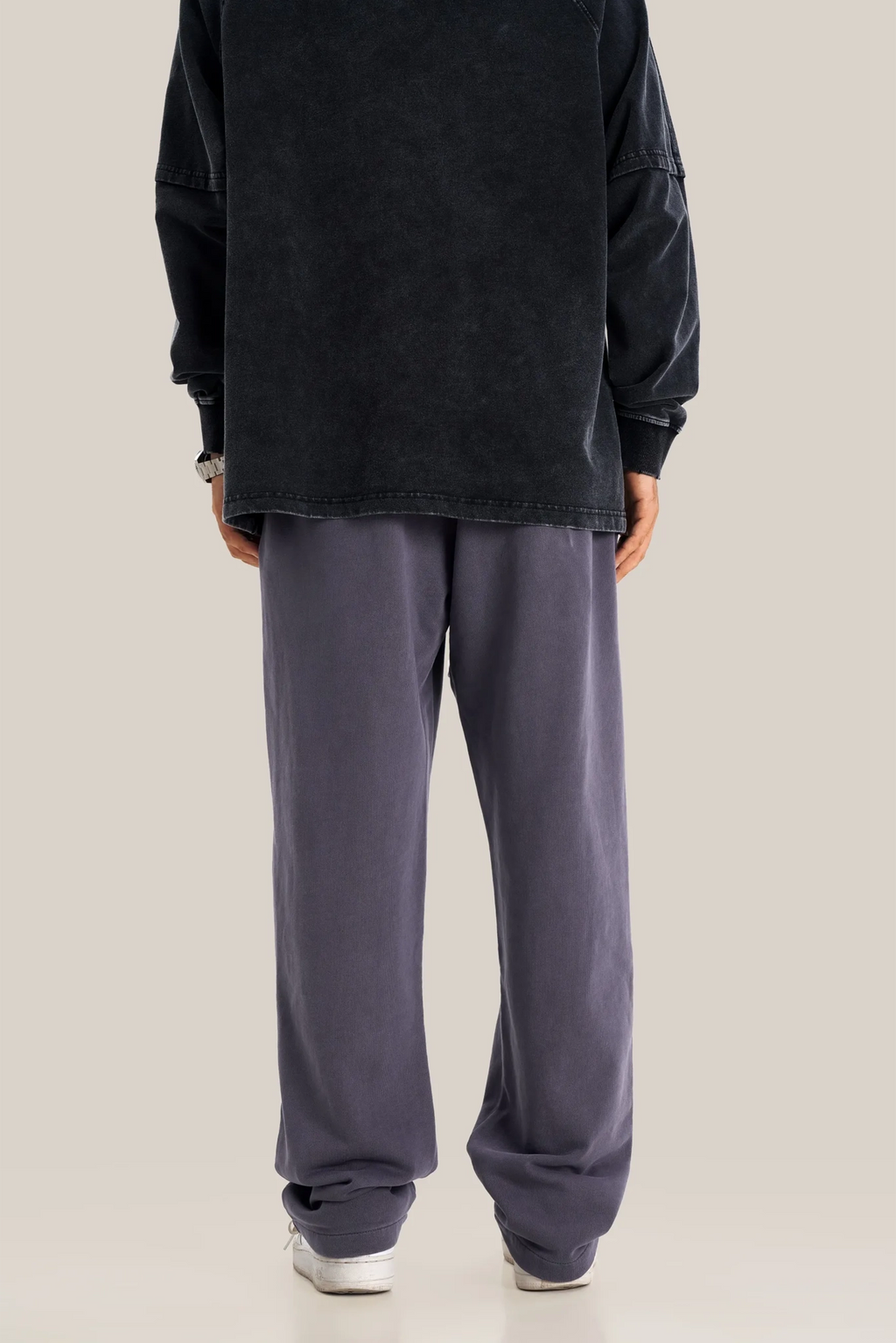 Person wearing a black oversized sweatshirt and gray sweatpants on a beige background