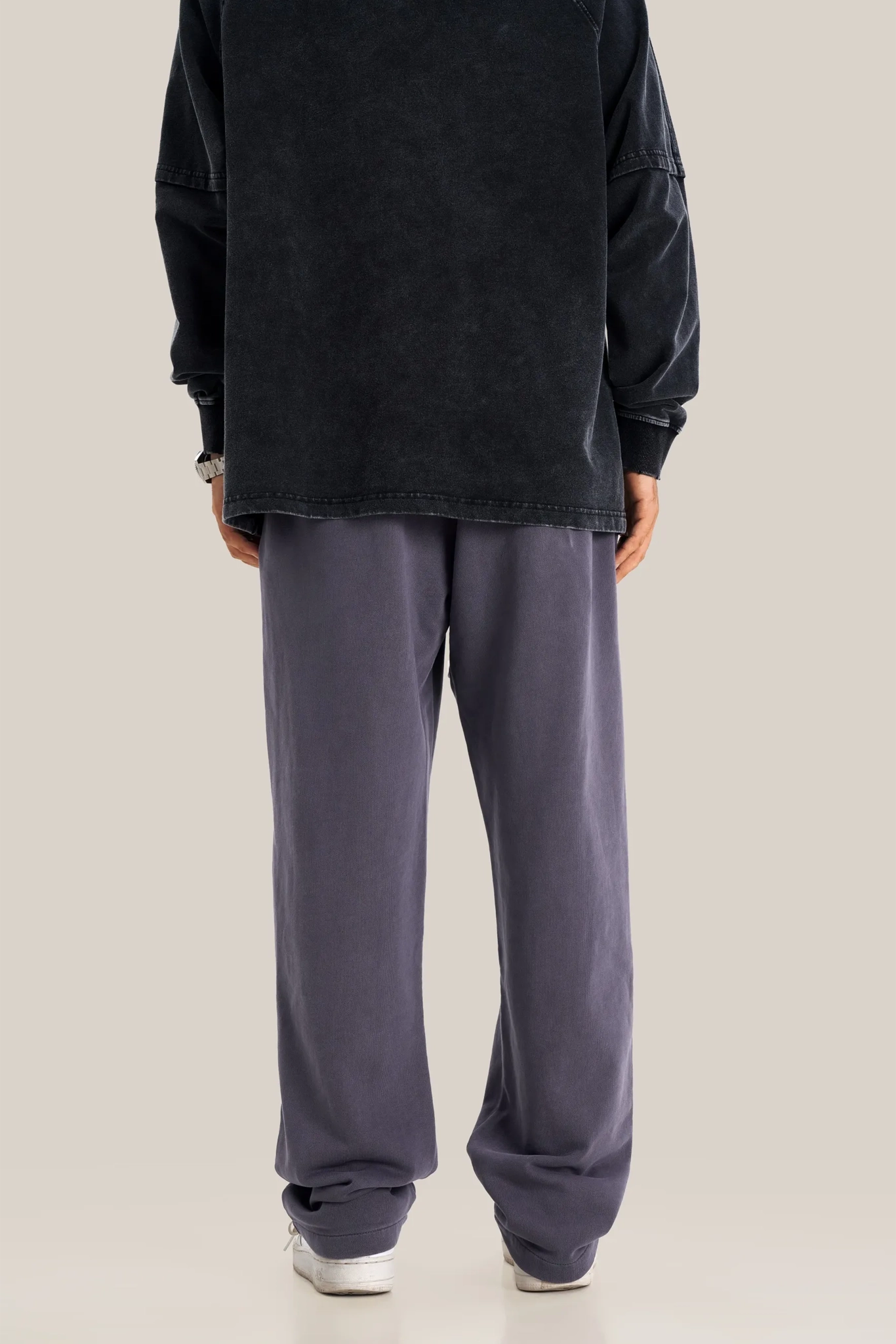 Person wearing a black oversized sweatshirt and gray sweatpants on a beige background