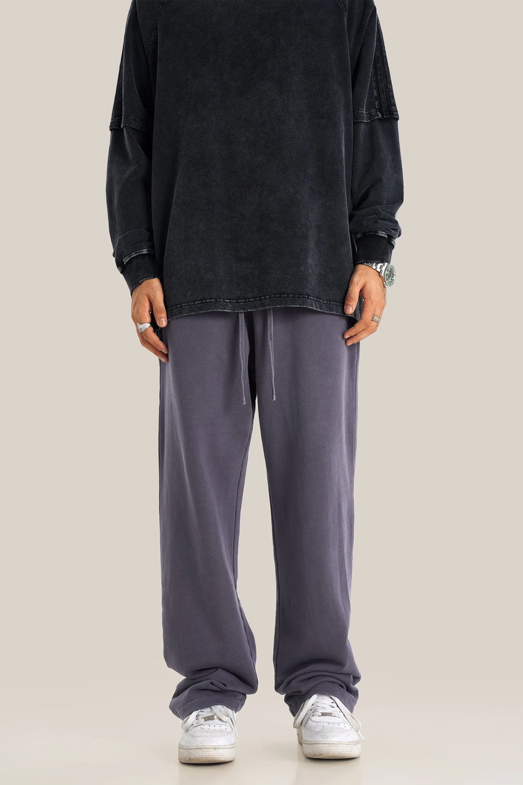 Person wearing a black oversized shirt and gray sweatpants on a beige background