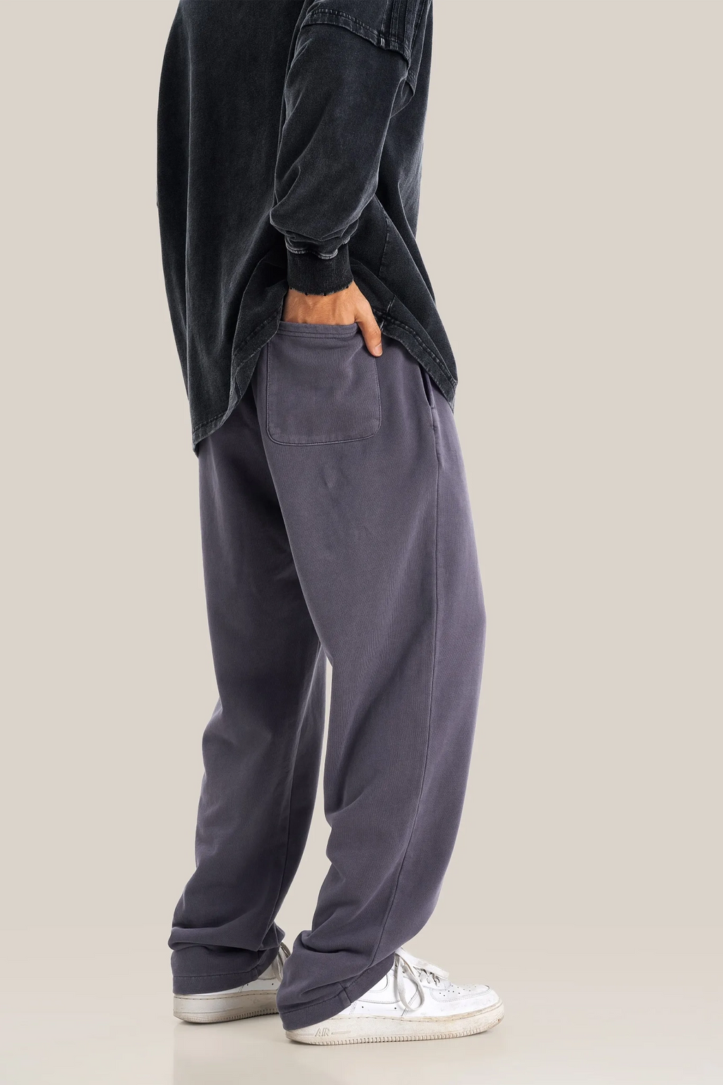 Person wearing dark gray sweatshirt and pants with white sneakers on a beige background