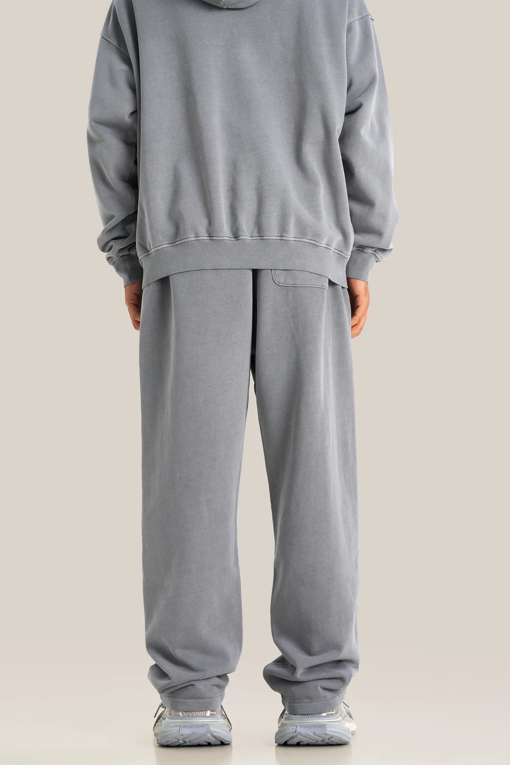 Person wearing a gray hoodie and pants on a beige background