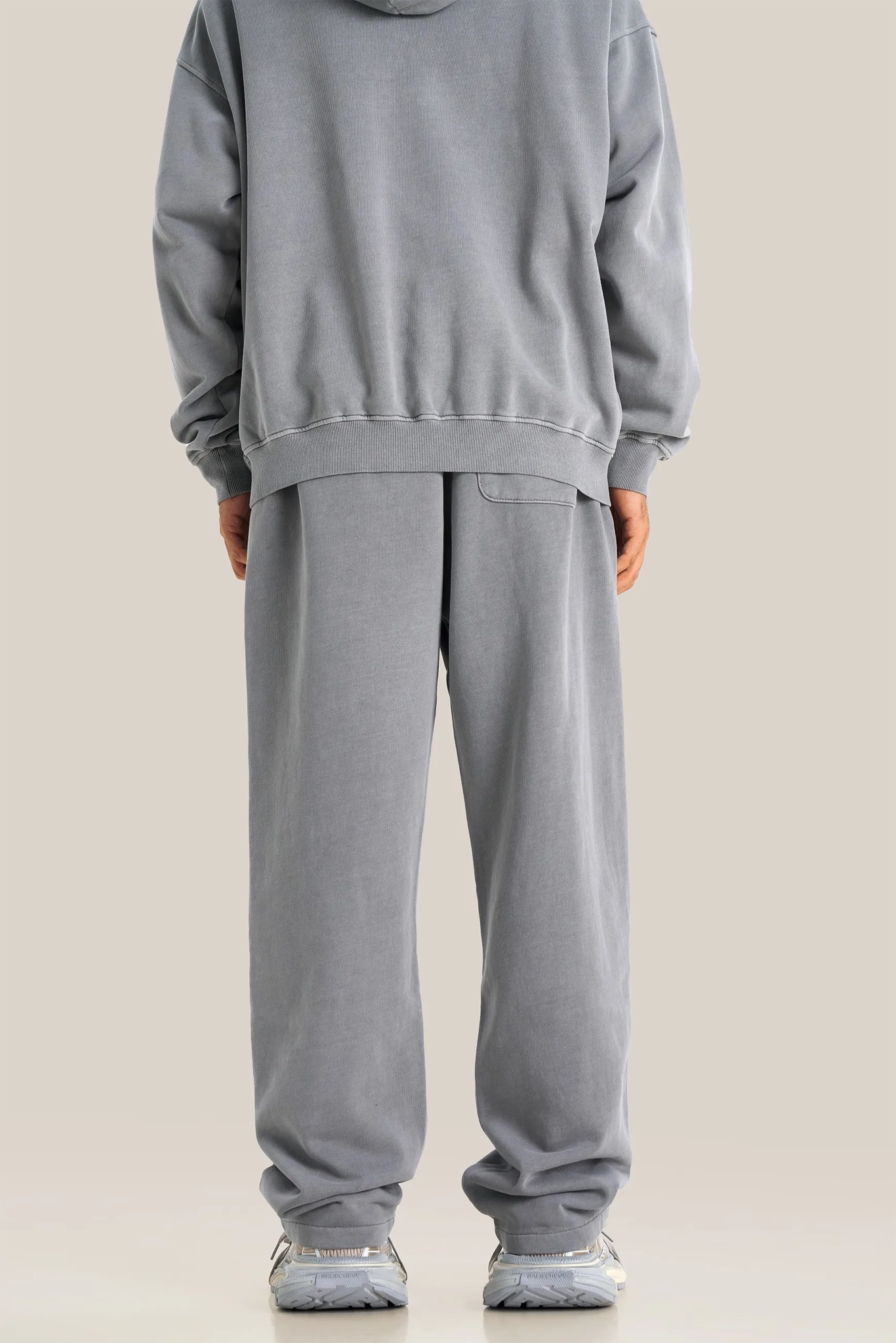 Person wearing a gray hoodie and pants on a beige background