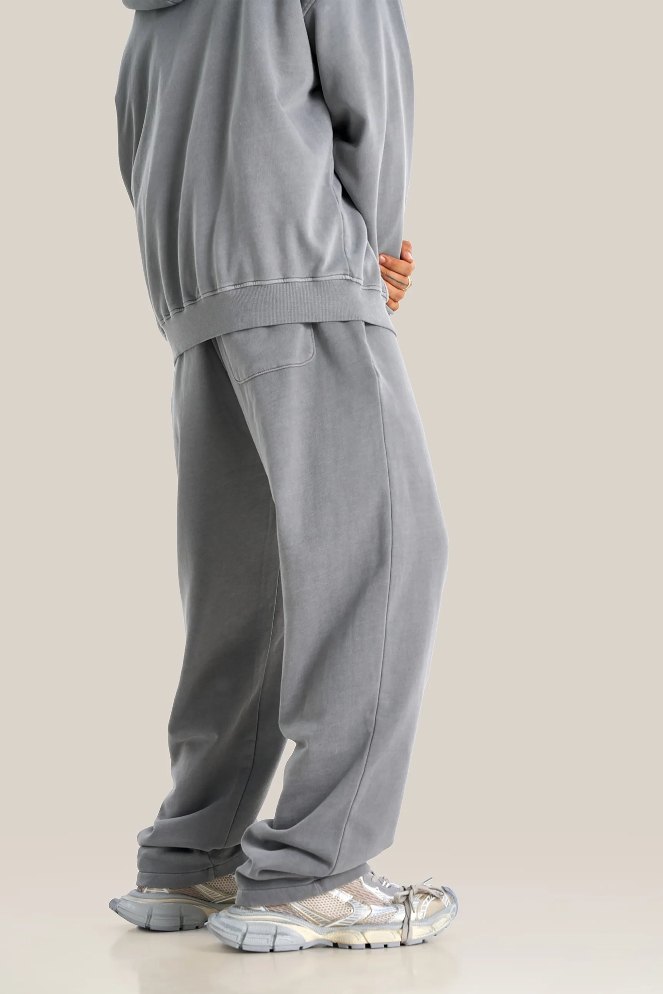 Person wearing a gray tracksuit with metallic shoes on a beige background