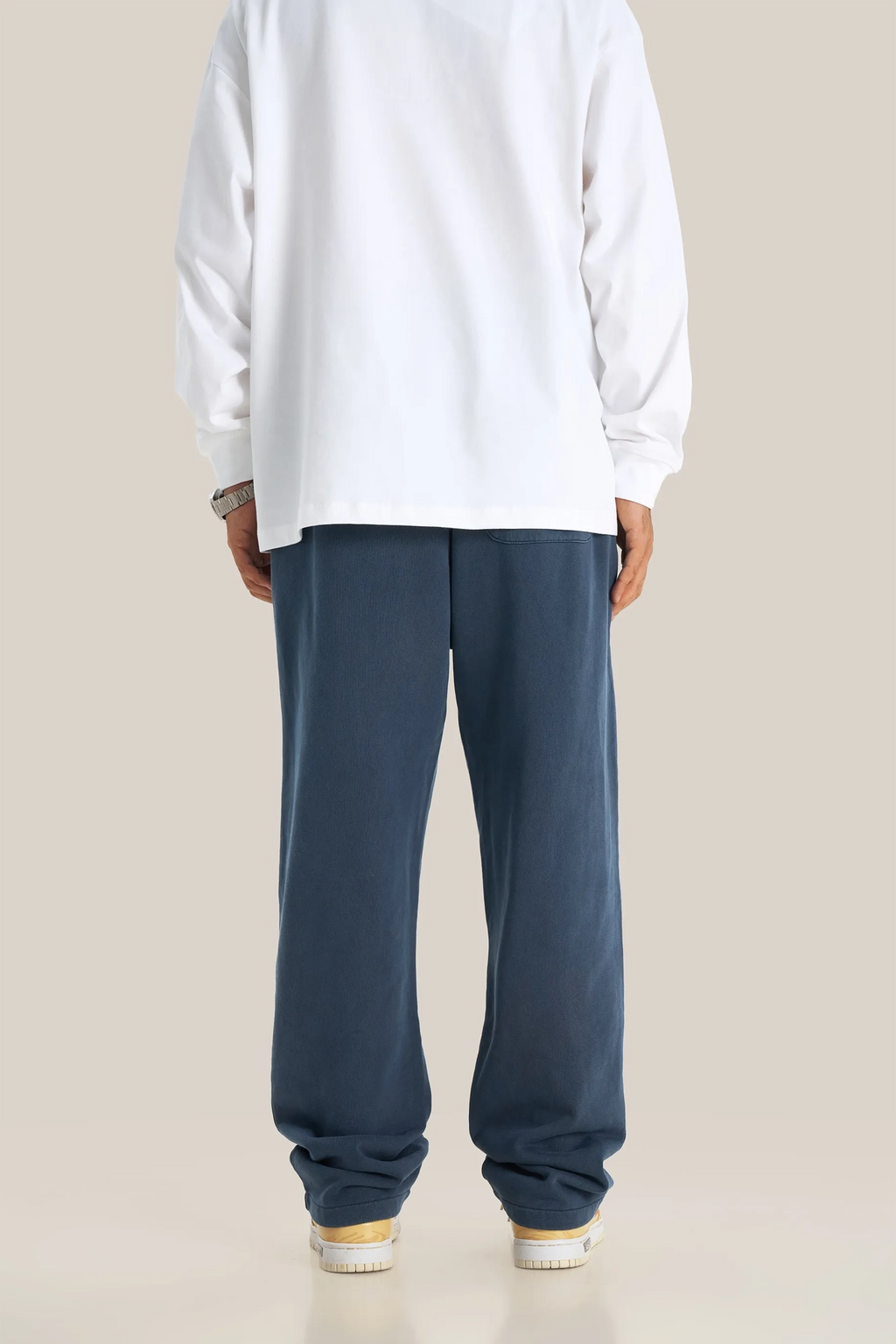 Person wearing a white sweatshirt and blue pants on a beige background