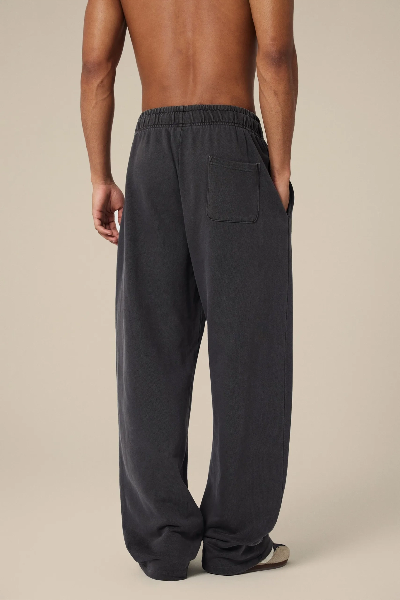 Person wearing dark gray sweatpants on a beige background