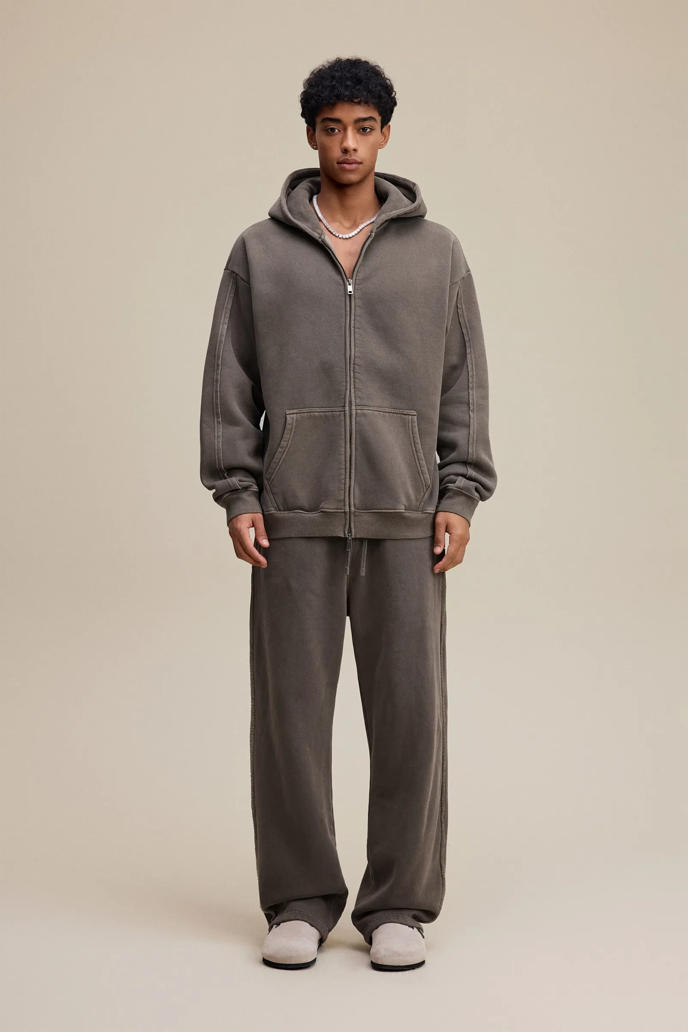 Person wearing a gray hoodie and pants on a beige background