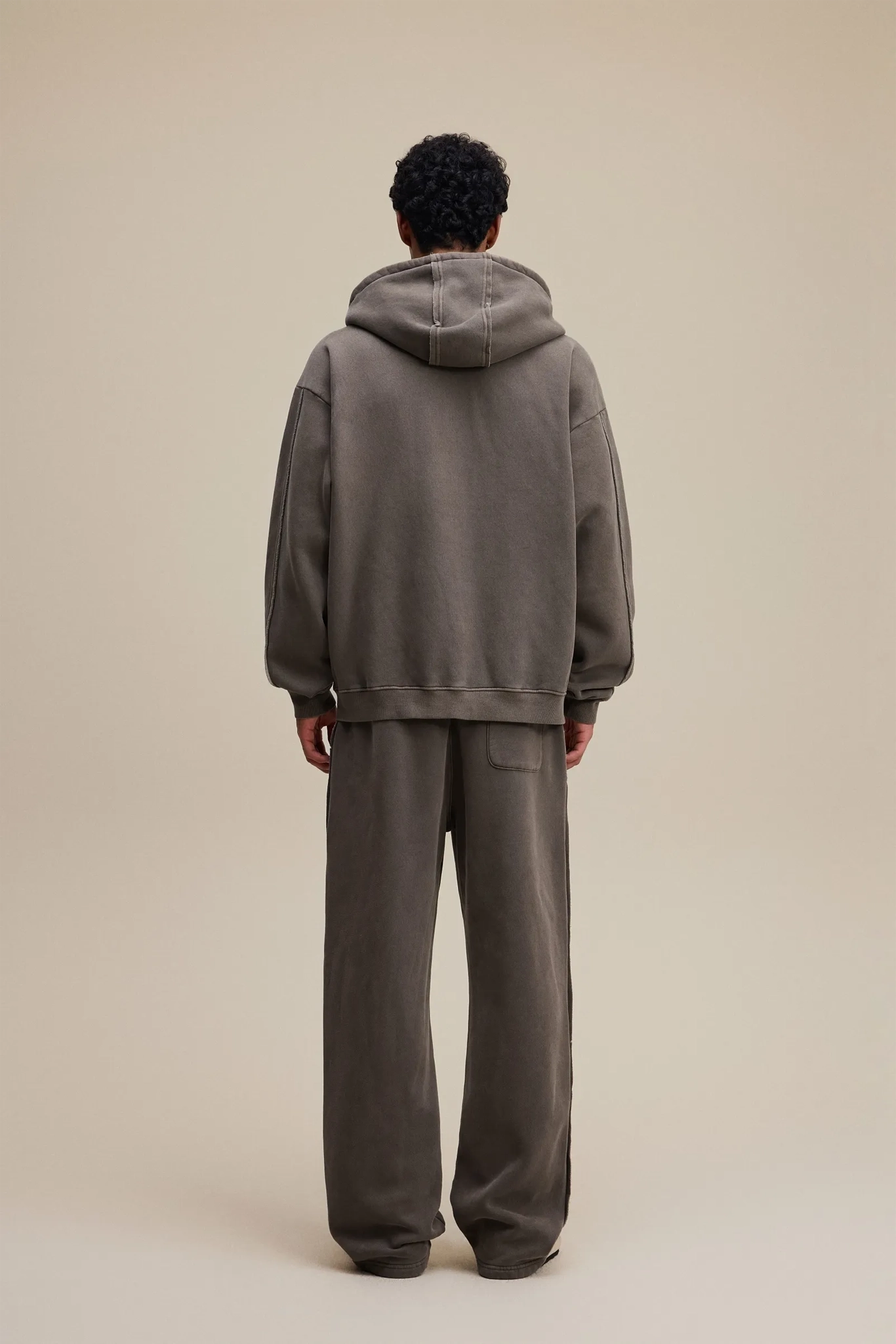 Person wearing a gray hoodie and pants on a beige background