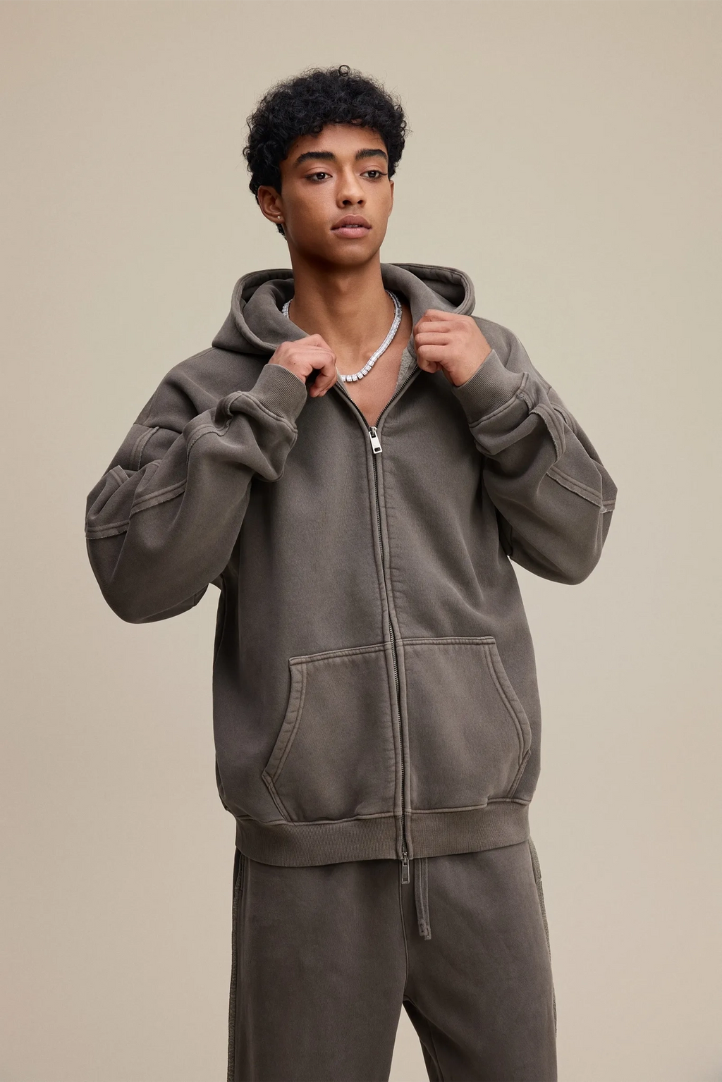 Person wearing a gray hoodie and pants on a beige background