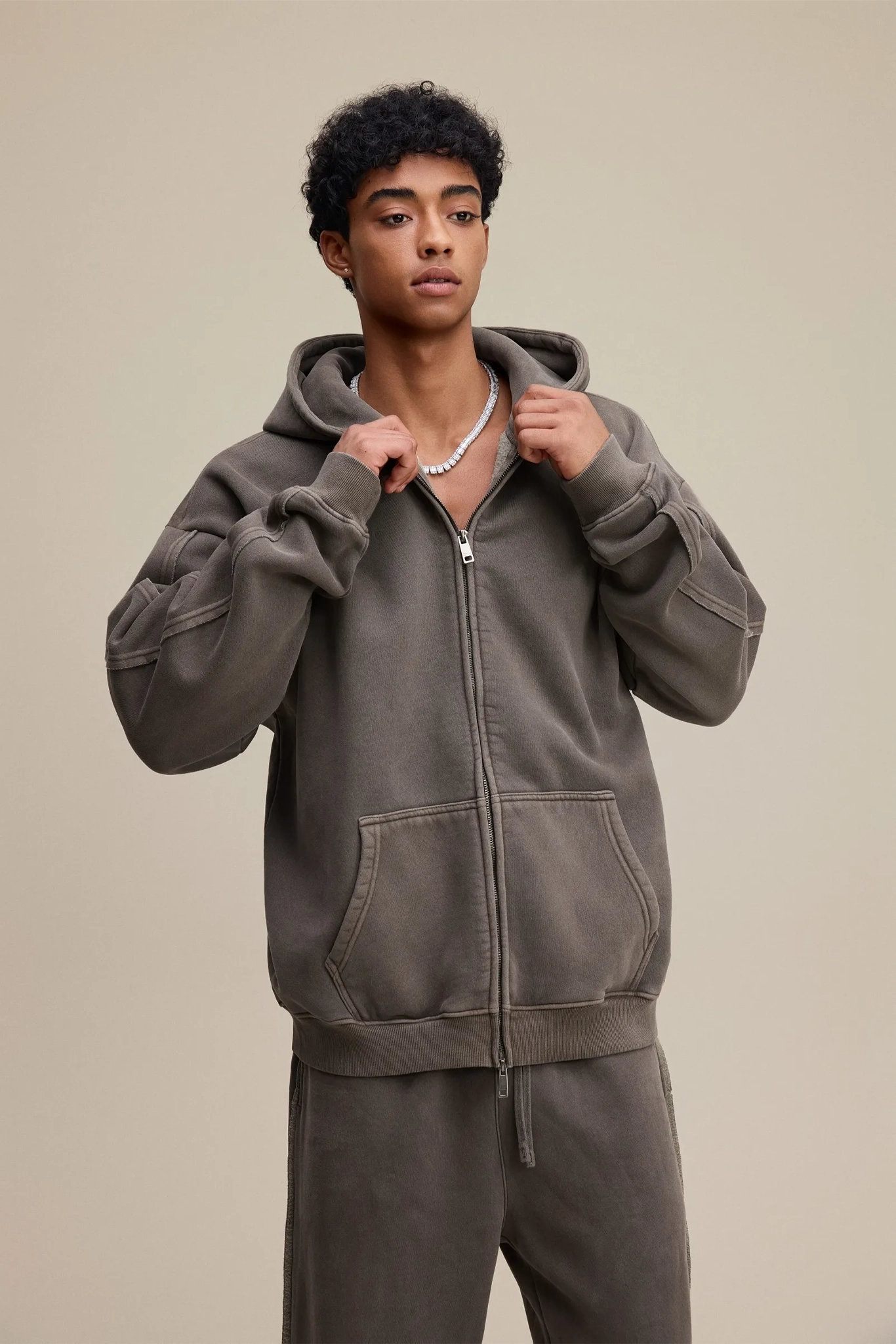 Person wearing a gray hoodie and pants on a beige background