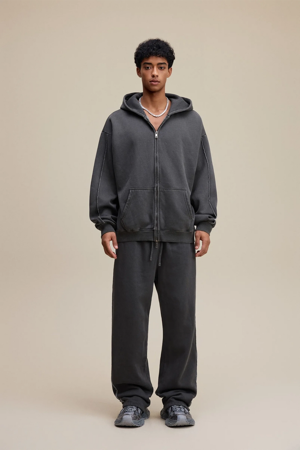 Person wearing a dark gray hoodie and pants on a beige background