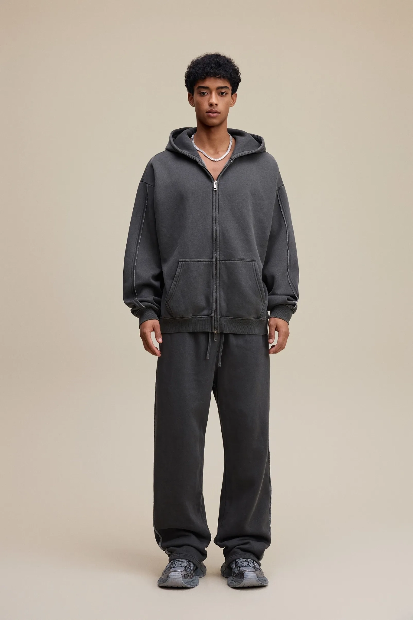 Person wearing a dark gray hoodie and pants on a beige background