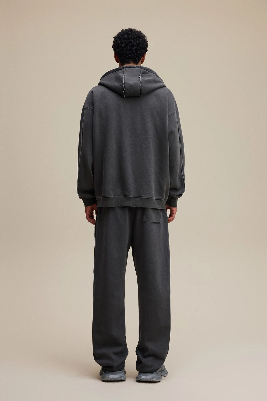 Person wearing a dark gray hoodie and pants on a beige background