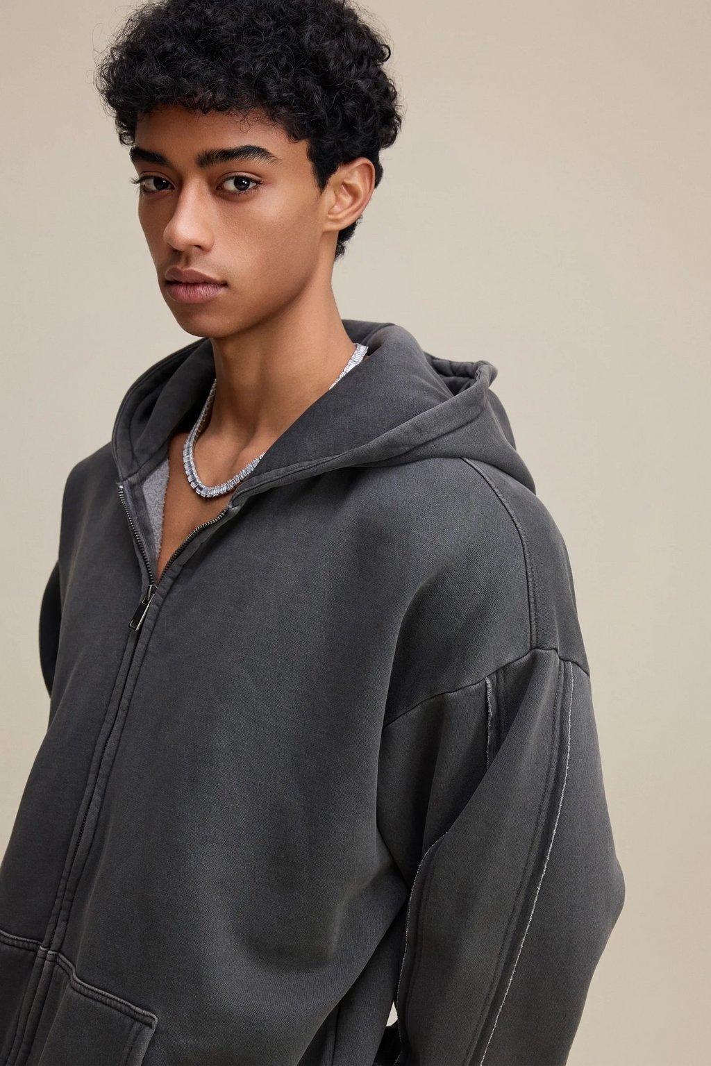 Person wearing a gray hoodie against a beige background