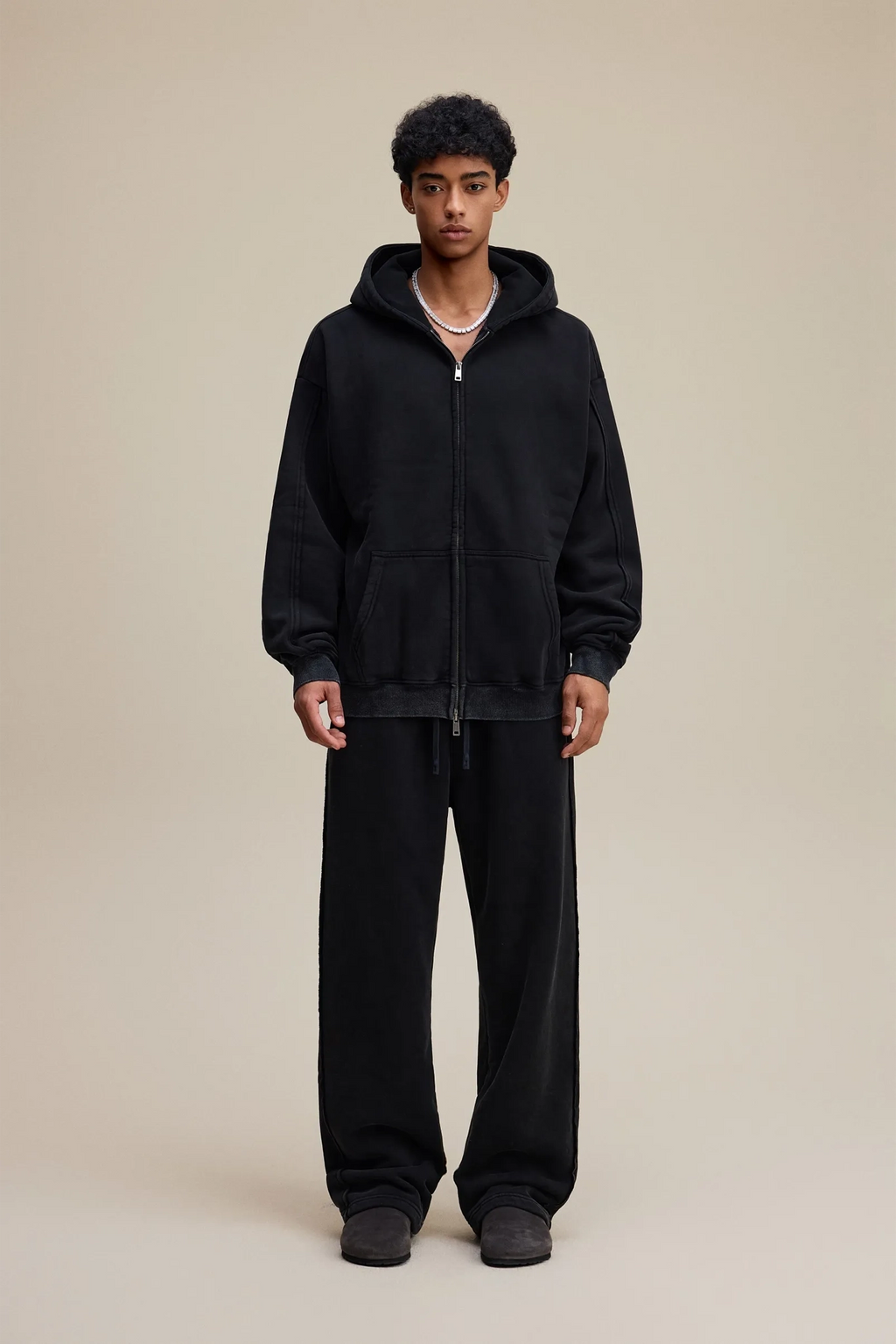 Person wearing a black hoodie and pants on a beige background