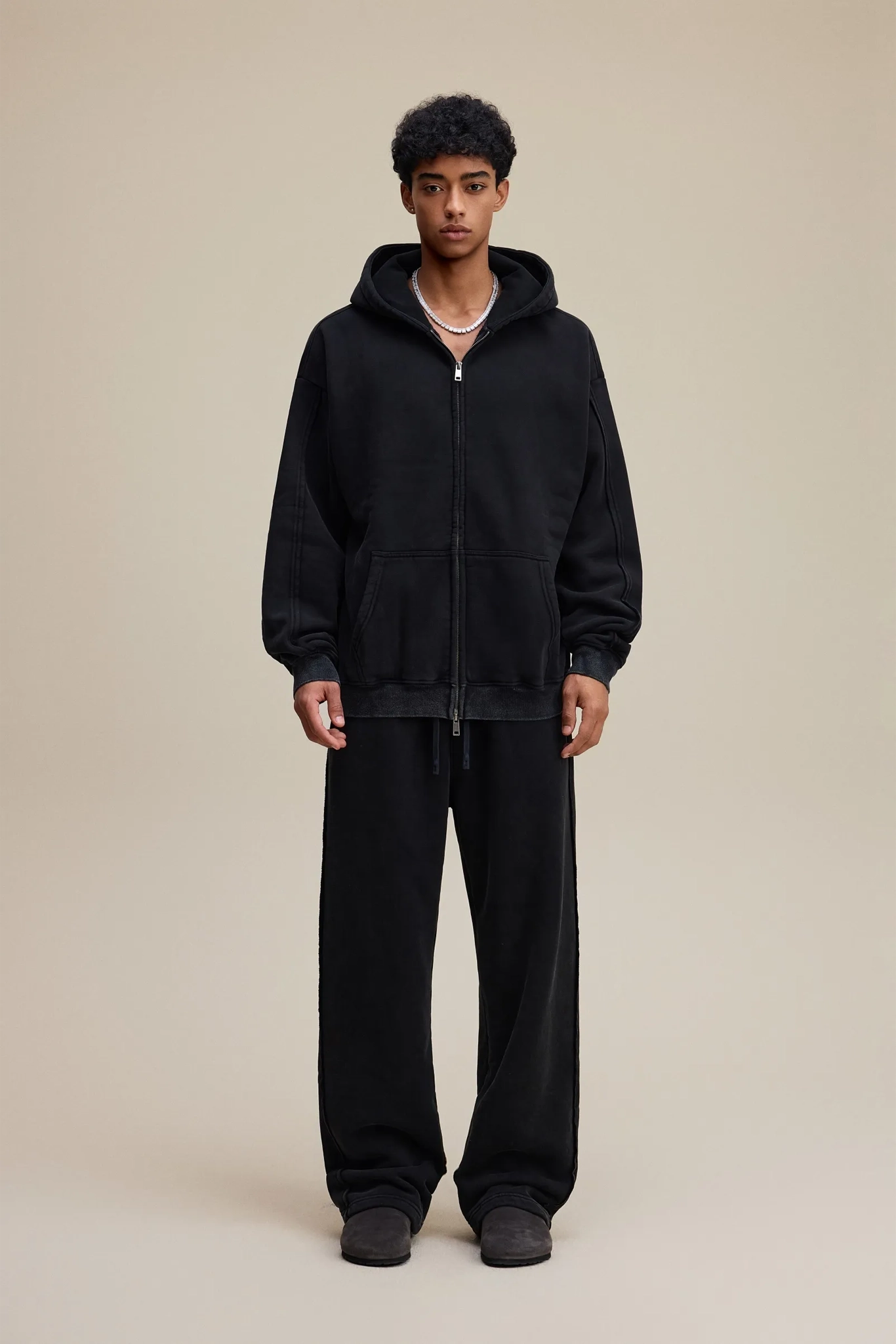 Person wearing a black hoodie and pants on a beige background