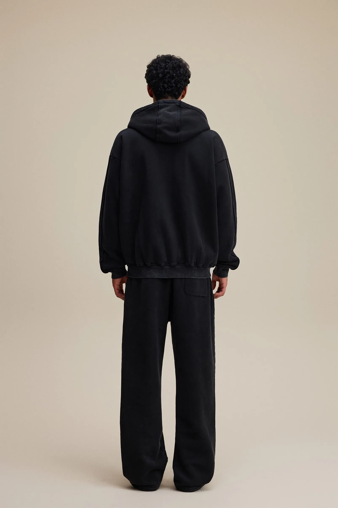 Person wearing a black hoodie and pants on a beige background