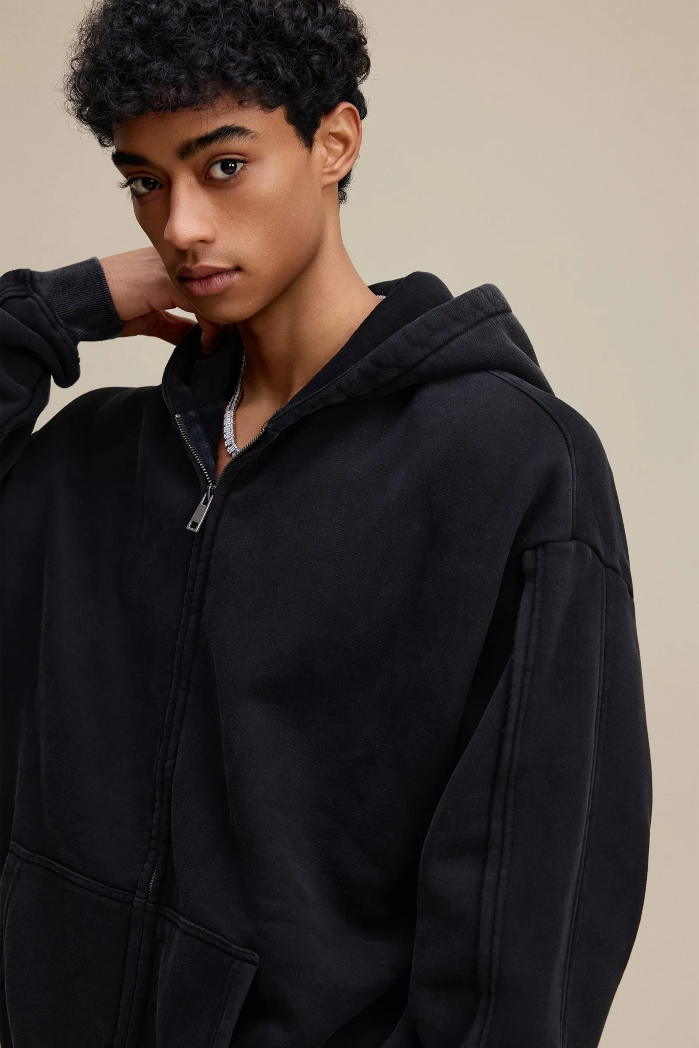 Person wearing a black hoodie against a beige background