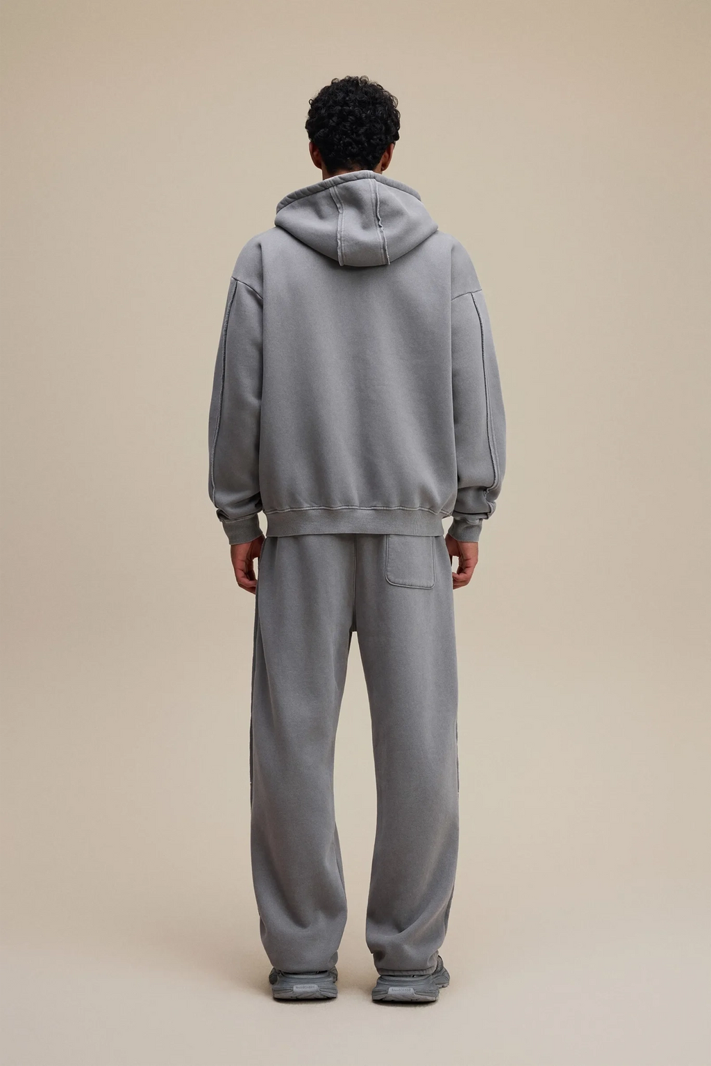 Person wearing a gray tracksuit against a beige background