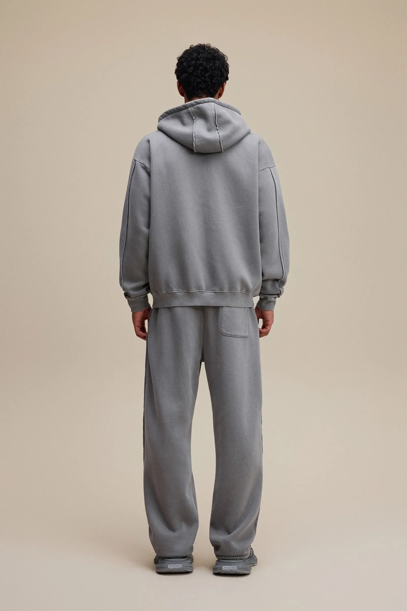 Person wearing a gray tracksuit against a beige background