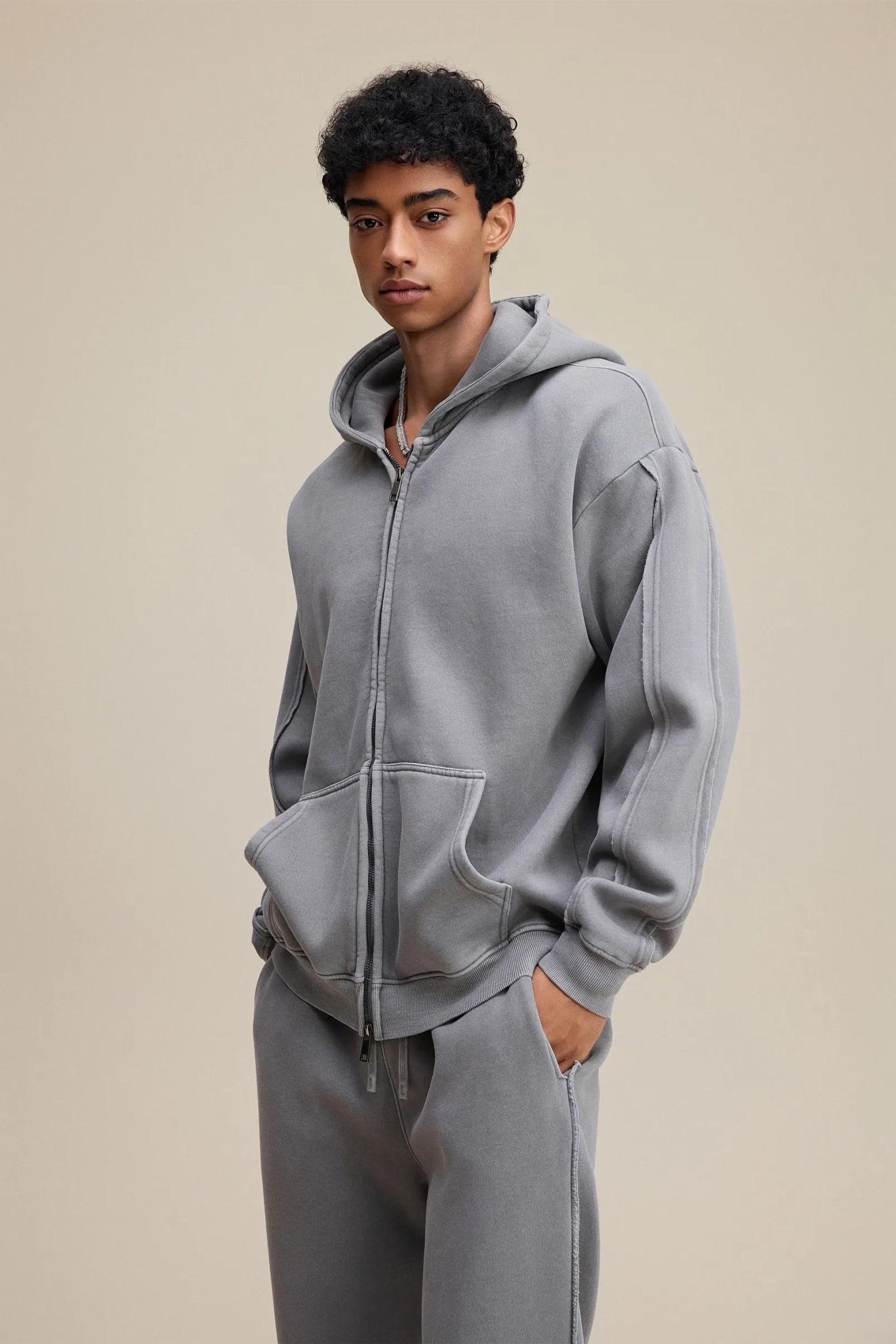 Person wearing a gray hoodie and pants on a beige background