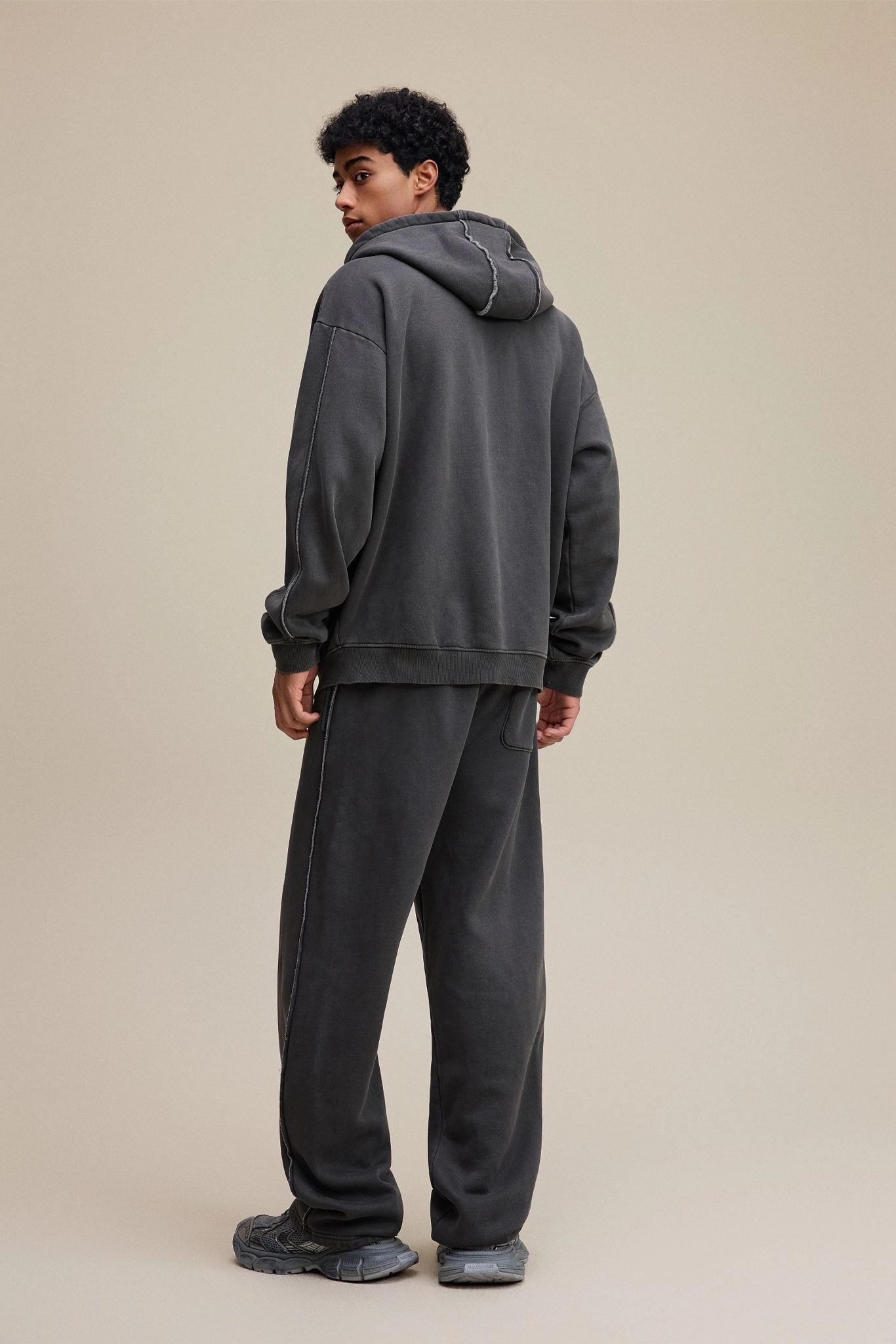 Person wearing a dark gray hoodie and pants on a beige background