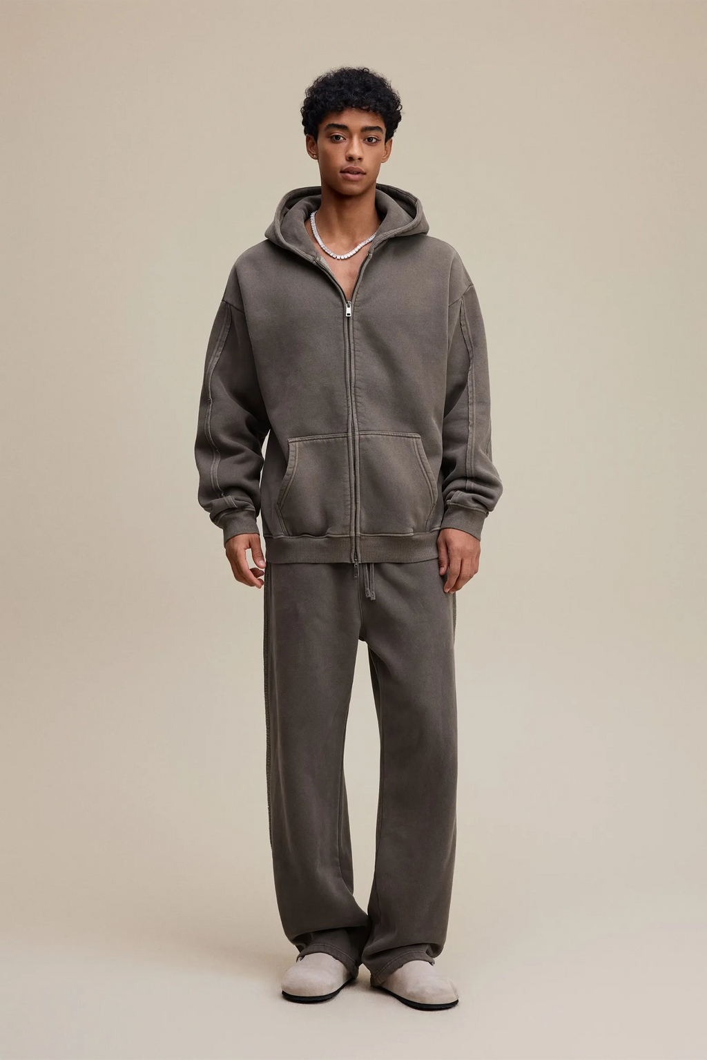 Person wearing a gray hoodie and pants set on a beige background