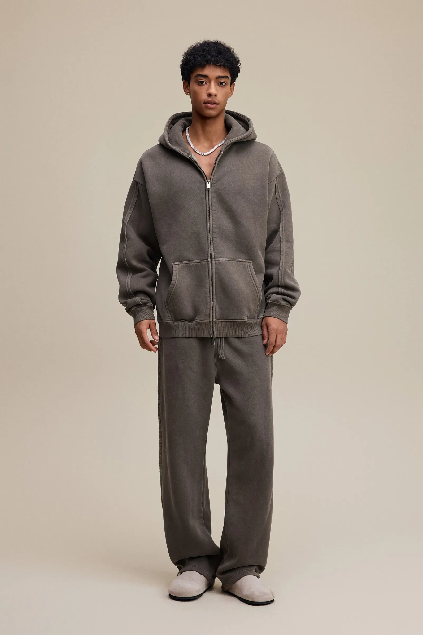 Person wearing a gray hoodie and pants set on a beige background