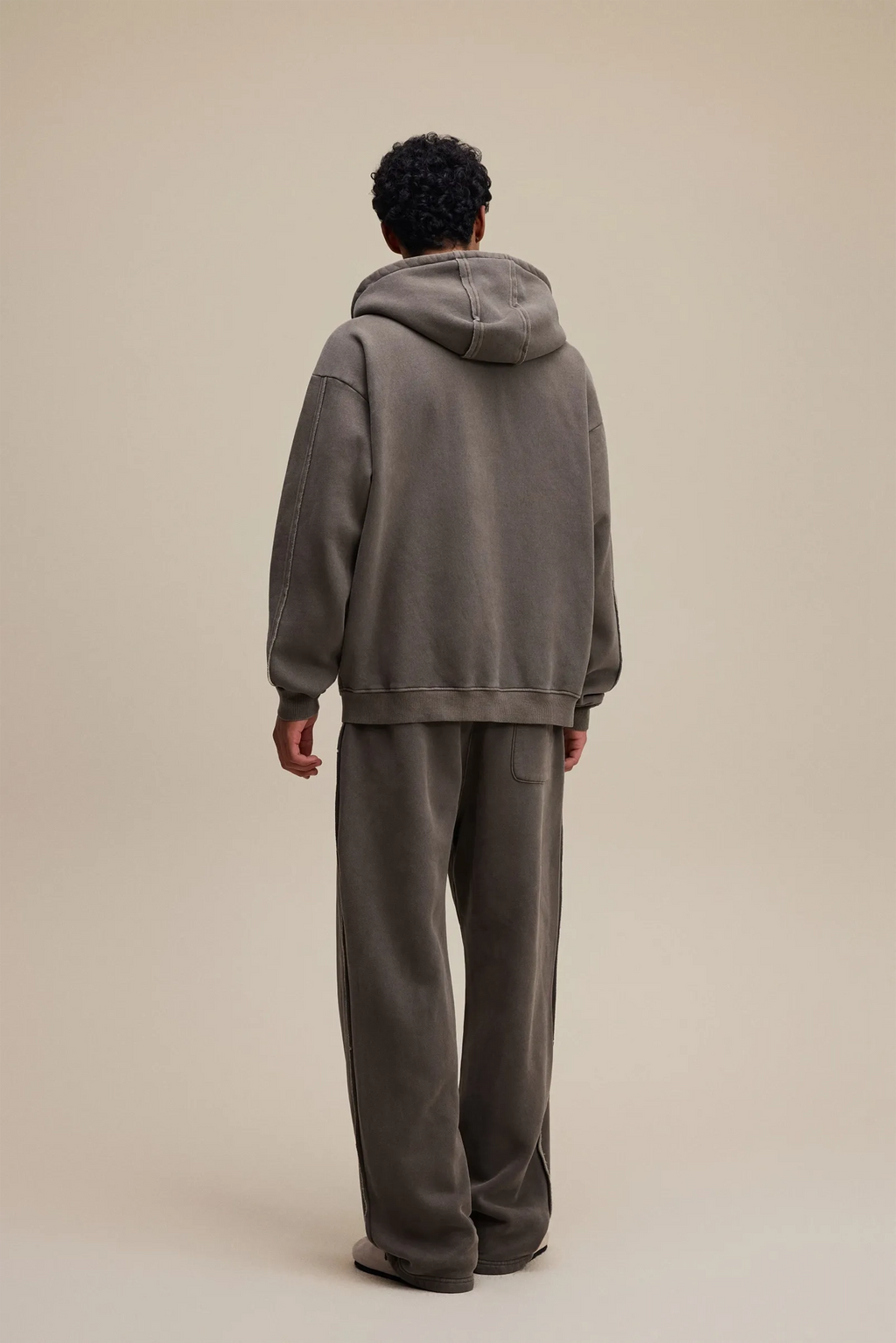 Person wearing a gray hoodie and pants on a beige background