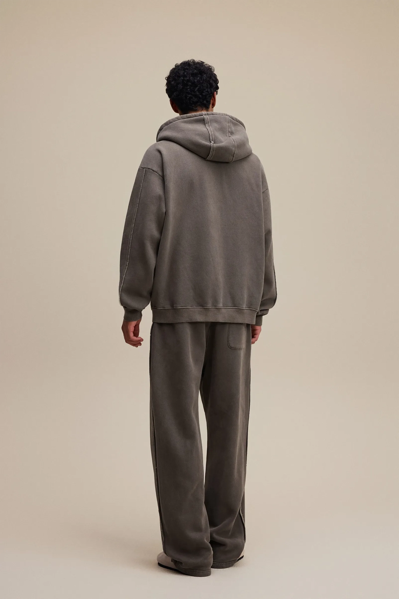 Person wearing a gray hoodie and pants on a beige background