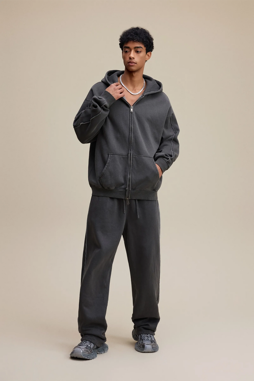 Person wearing a dark gray hoodie and pants on a beige background