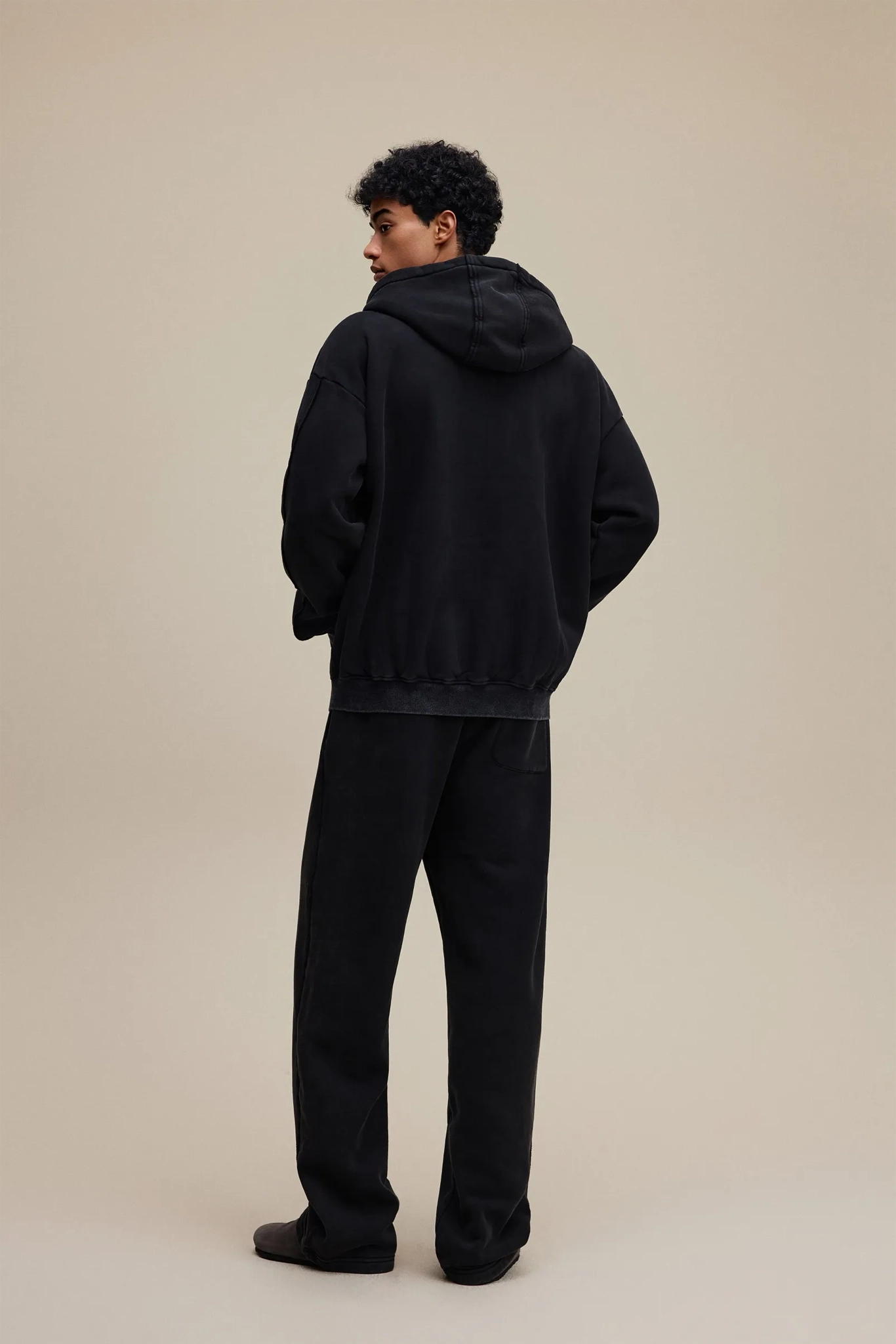 Person wearing a black hoodie and pants on a beige background