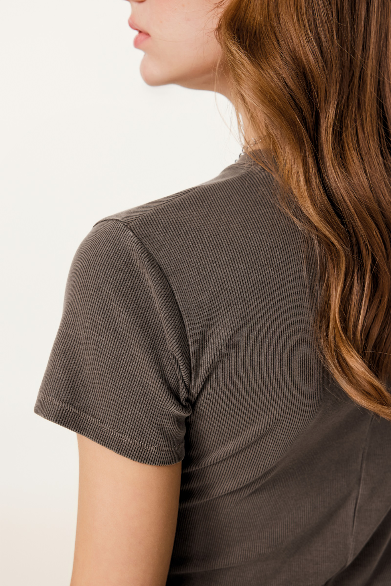 Person wearing a brown ribbed t-shirt on a plain background