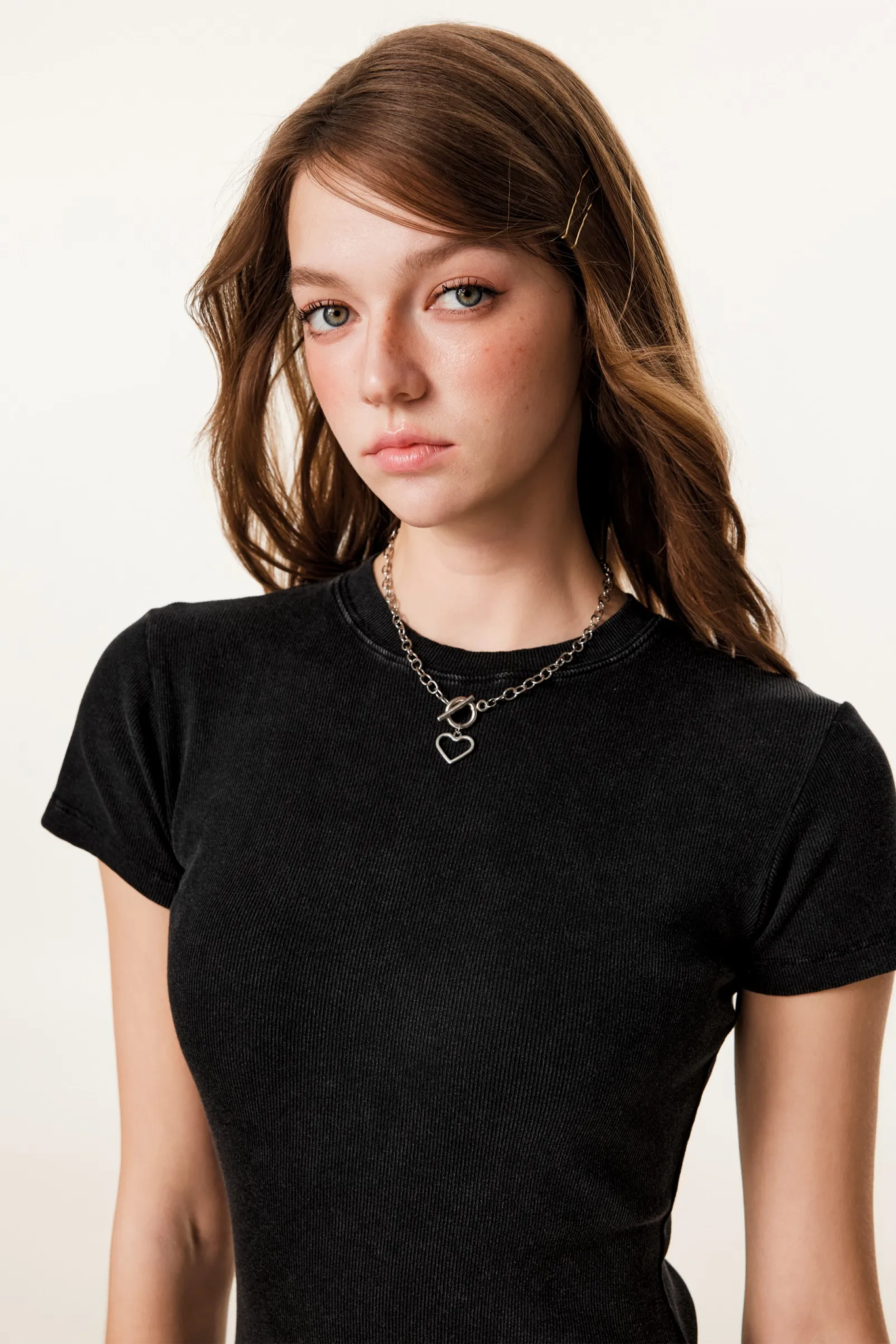 Person wearing a black t-shirt with a necklace on a plain background