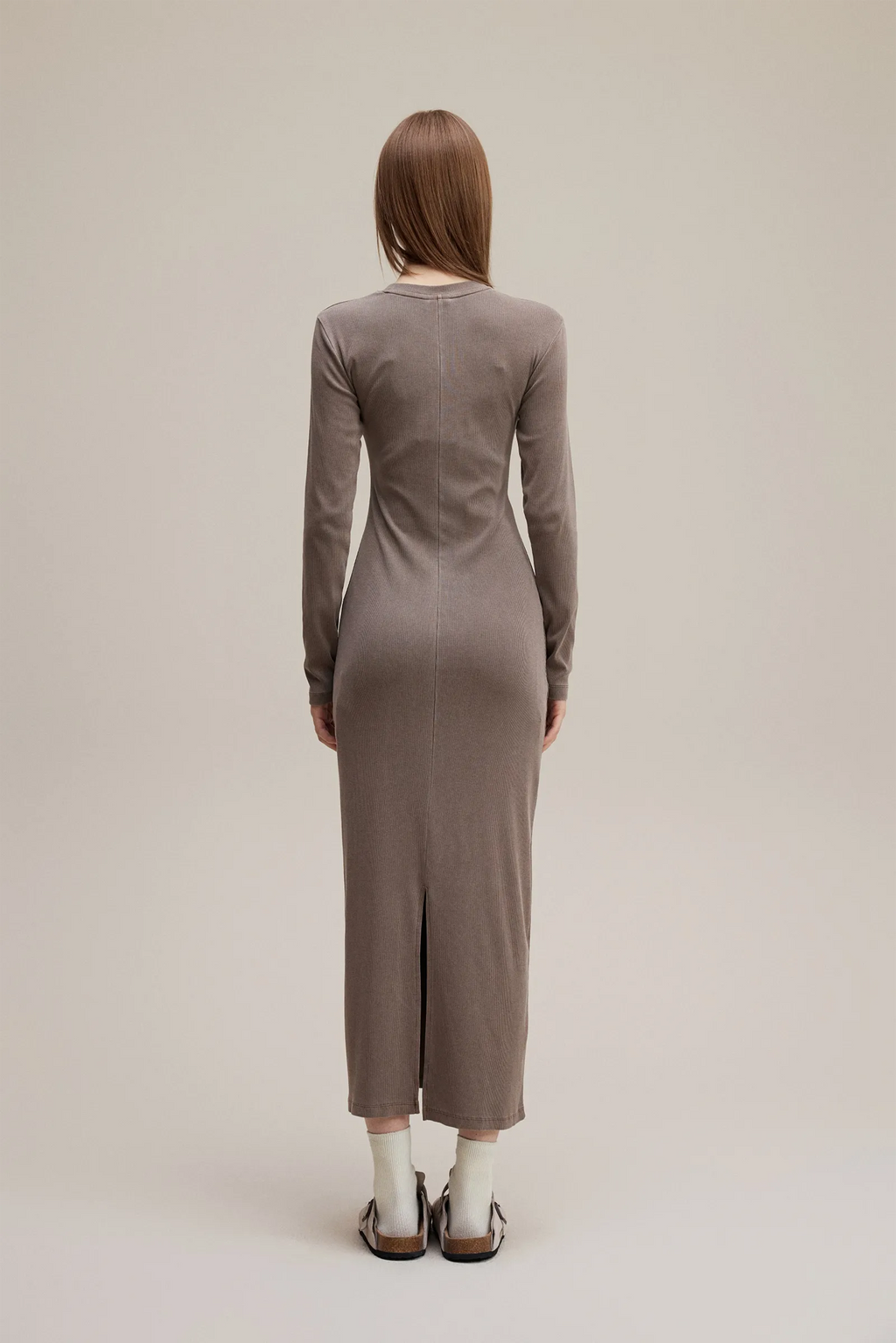 Person wearing a long-sleeve, knee-length dress in a neutral color on a plain background